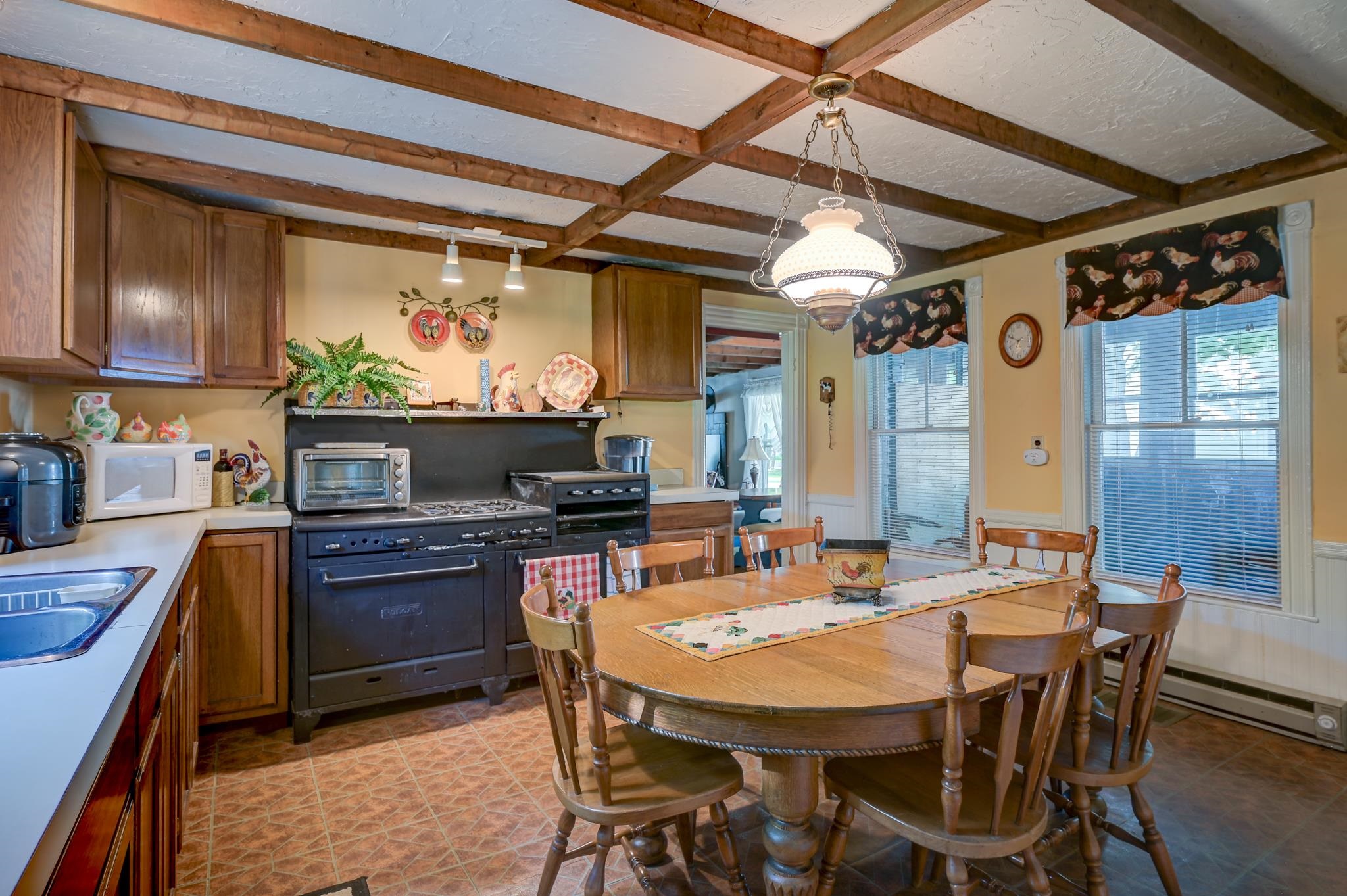 Kitchen with exposed ceiling beams, a large black range, and an oval dining table beside two windows.
