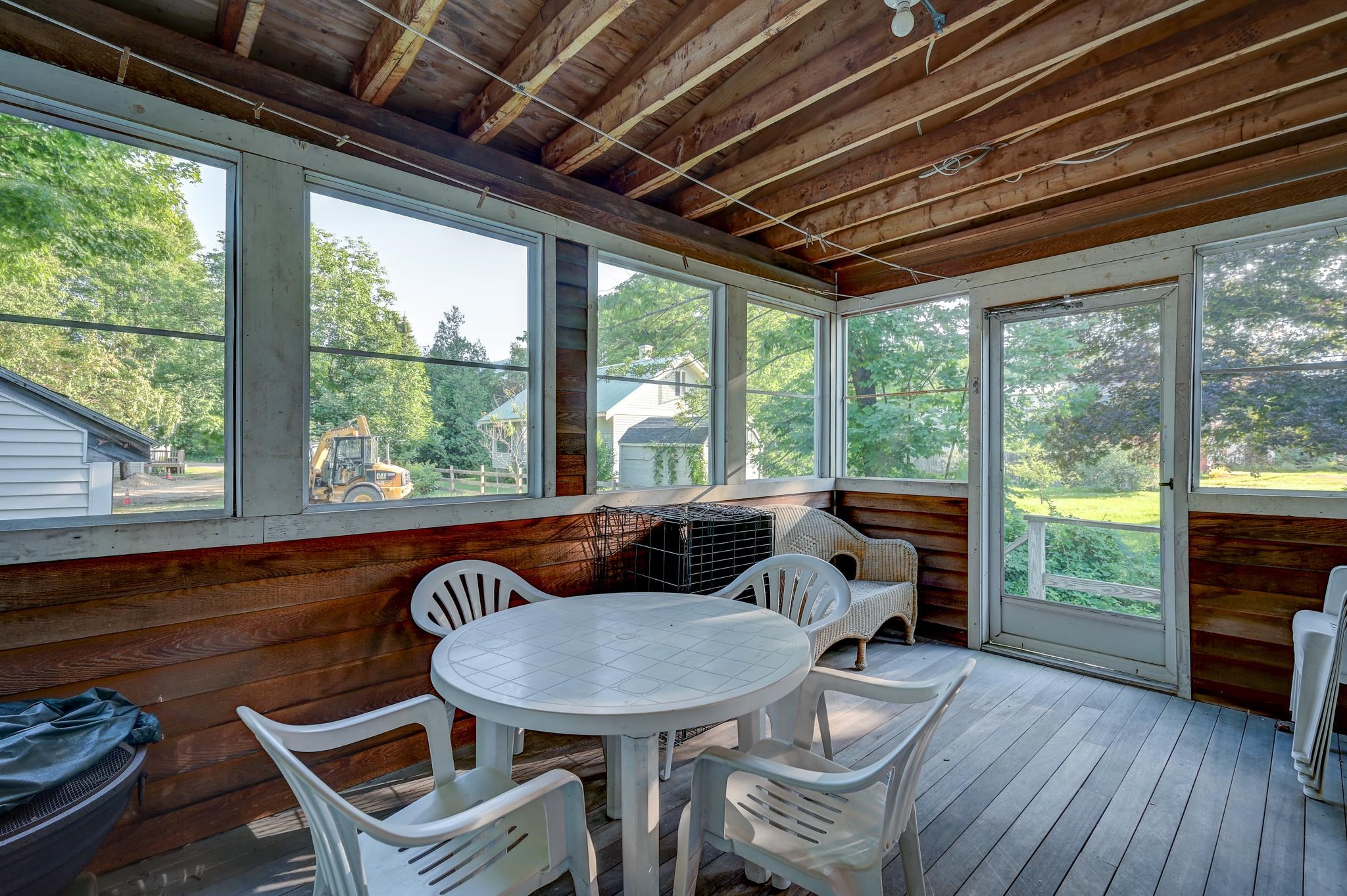 Enclosed porch with exposed beams, broad windows, and a white patio table and chairs.