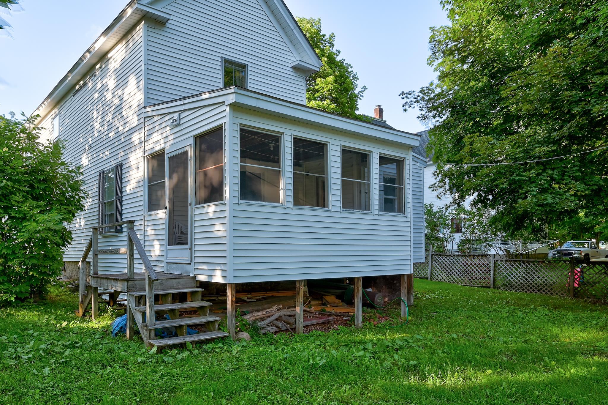 White clapboard house with a raised enclosed porch and wooden steps in a leafy yard.