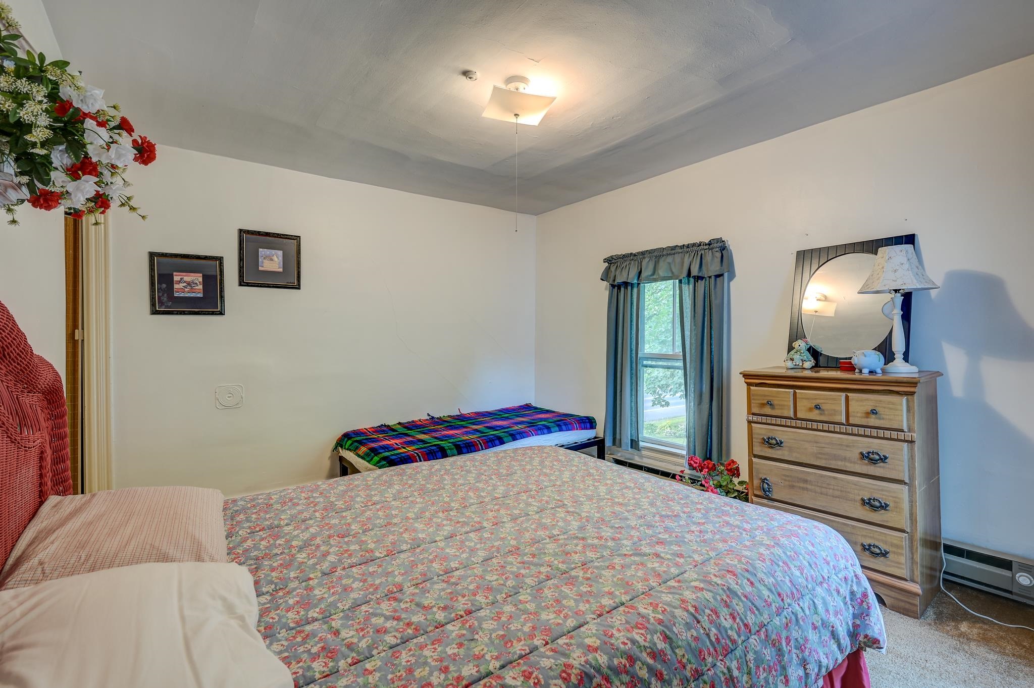Bedroom with floral bedspreads, blue curtains, and a wooden dresser with a round mirror.