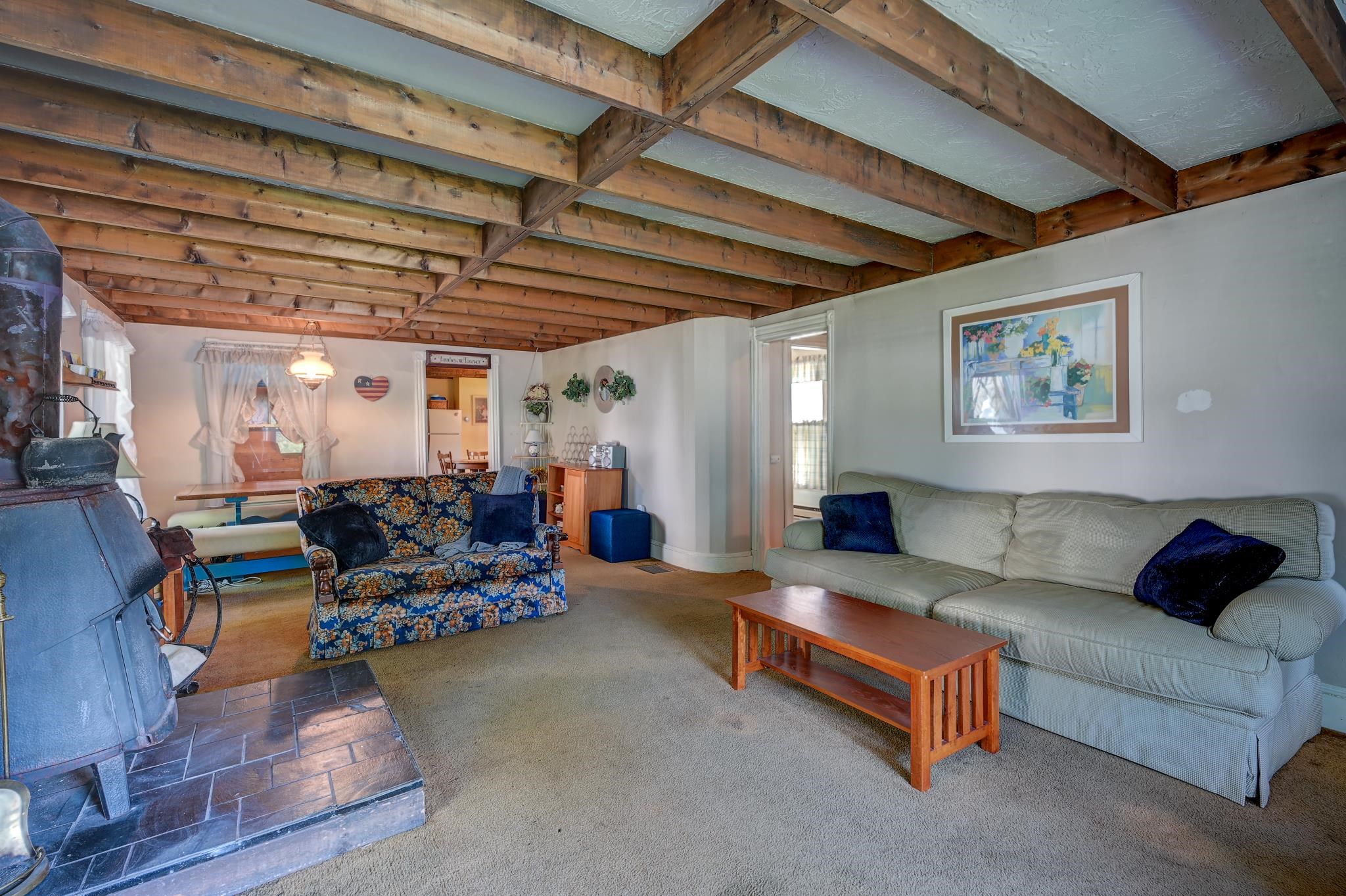 Living room with exposed wood beams, a wood stove, and two sofas.