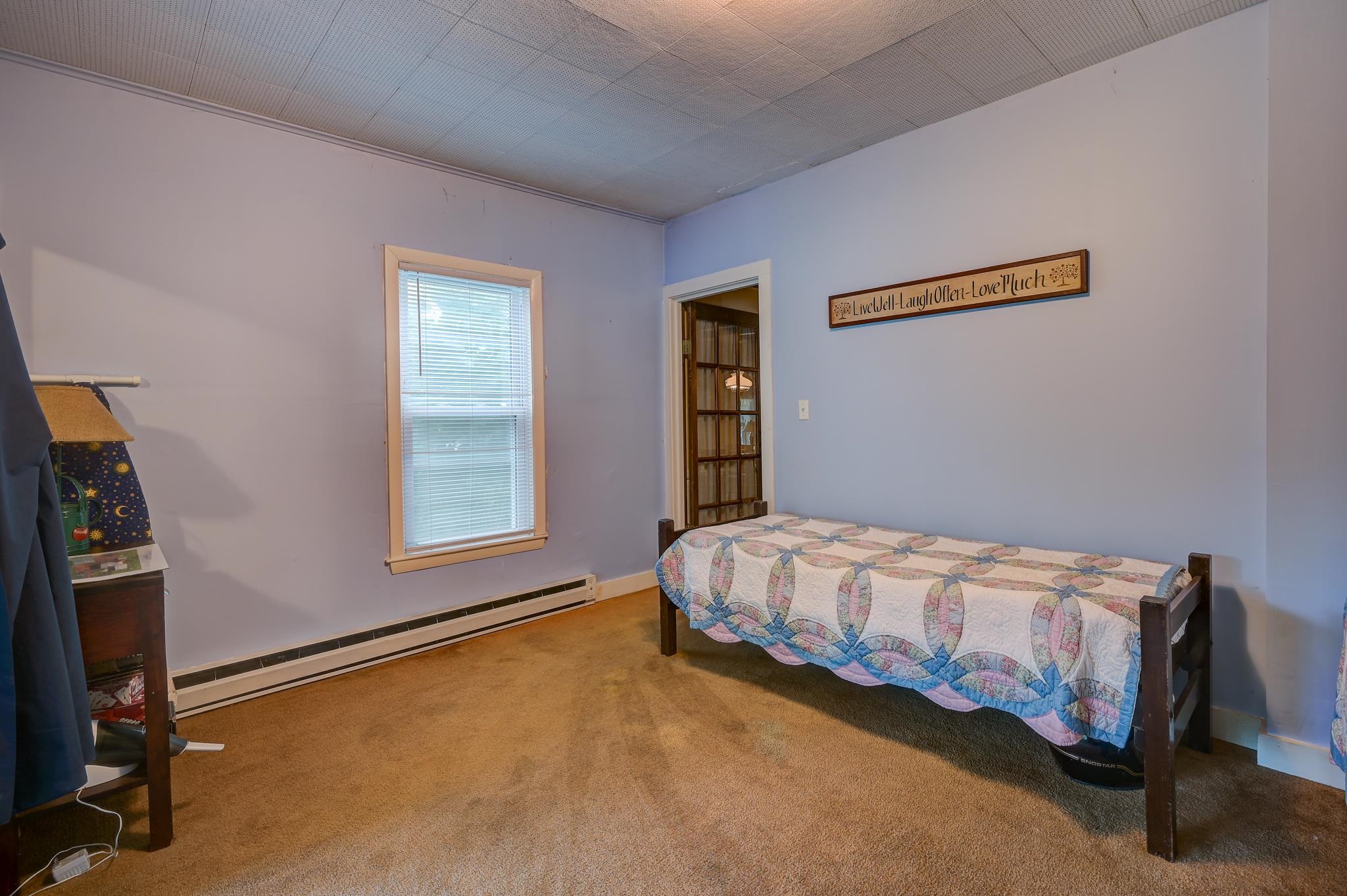 Bedroom with a single bed under a colorful quilt and a window with blinds.