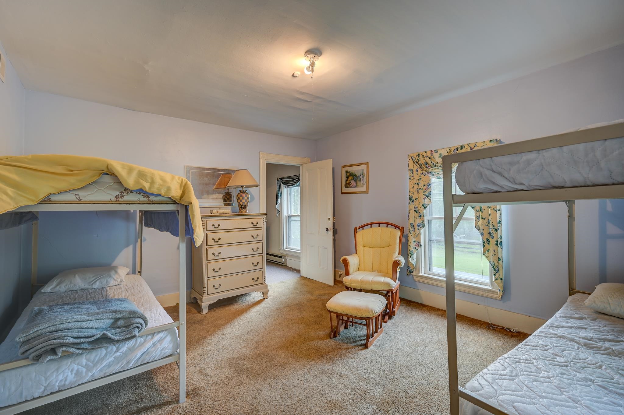 Bedroom with two bunk beds, a cream dresser, and a yellow rocking chair beside curtained windows.