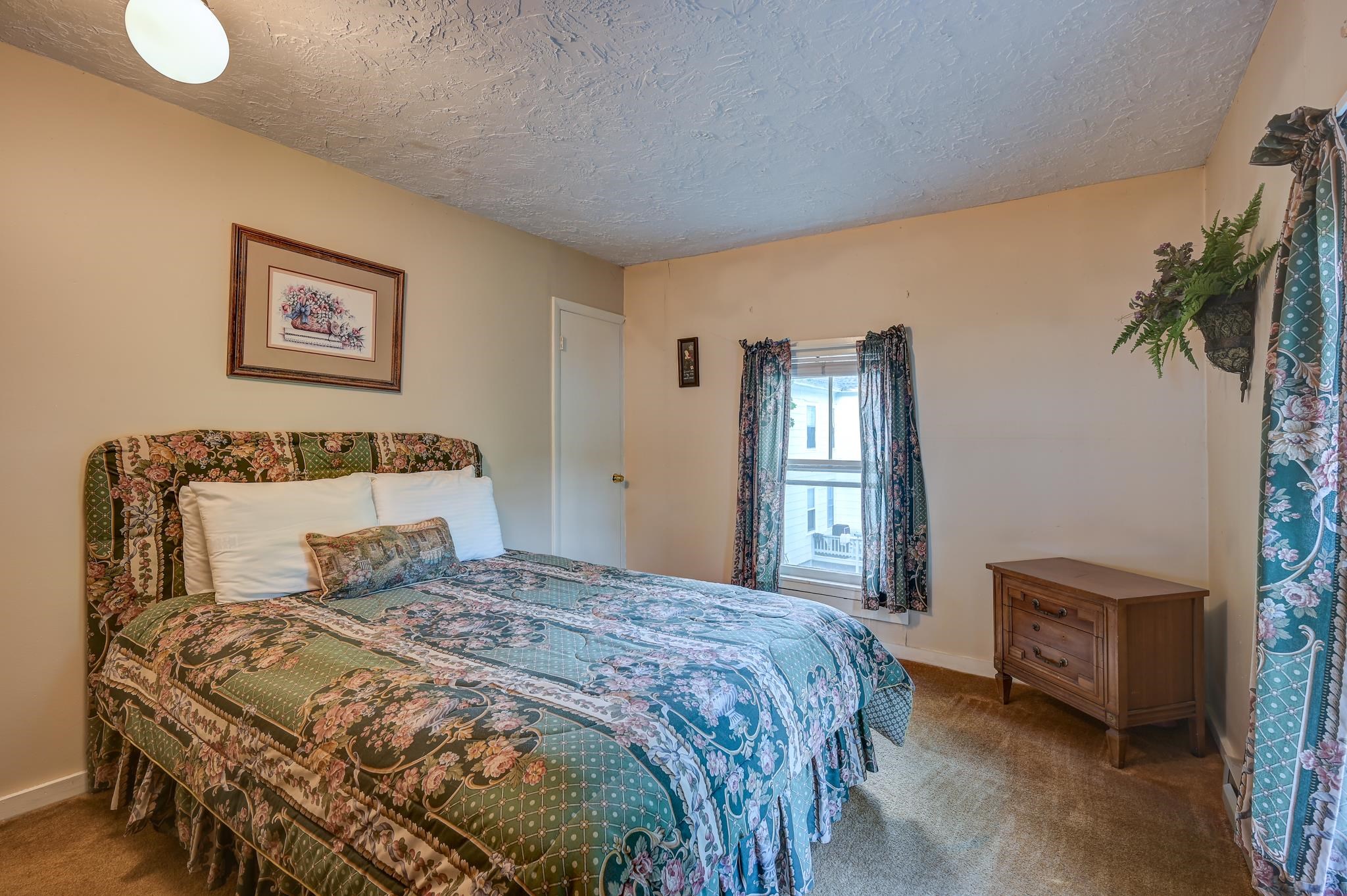 Furnished bedroom with a large floral bed, matching curtains, and a wooden dresser.