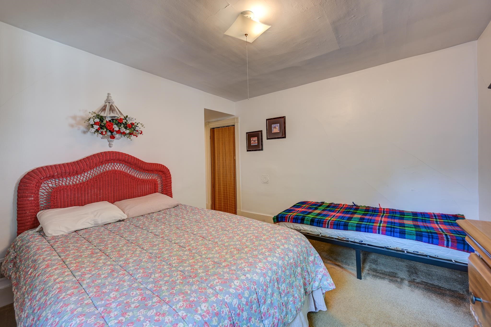Bedroom with a red wicker headboard, floral bedding, and a narrow bed with a plaid blanket.