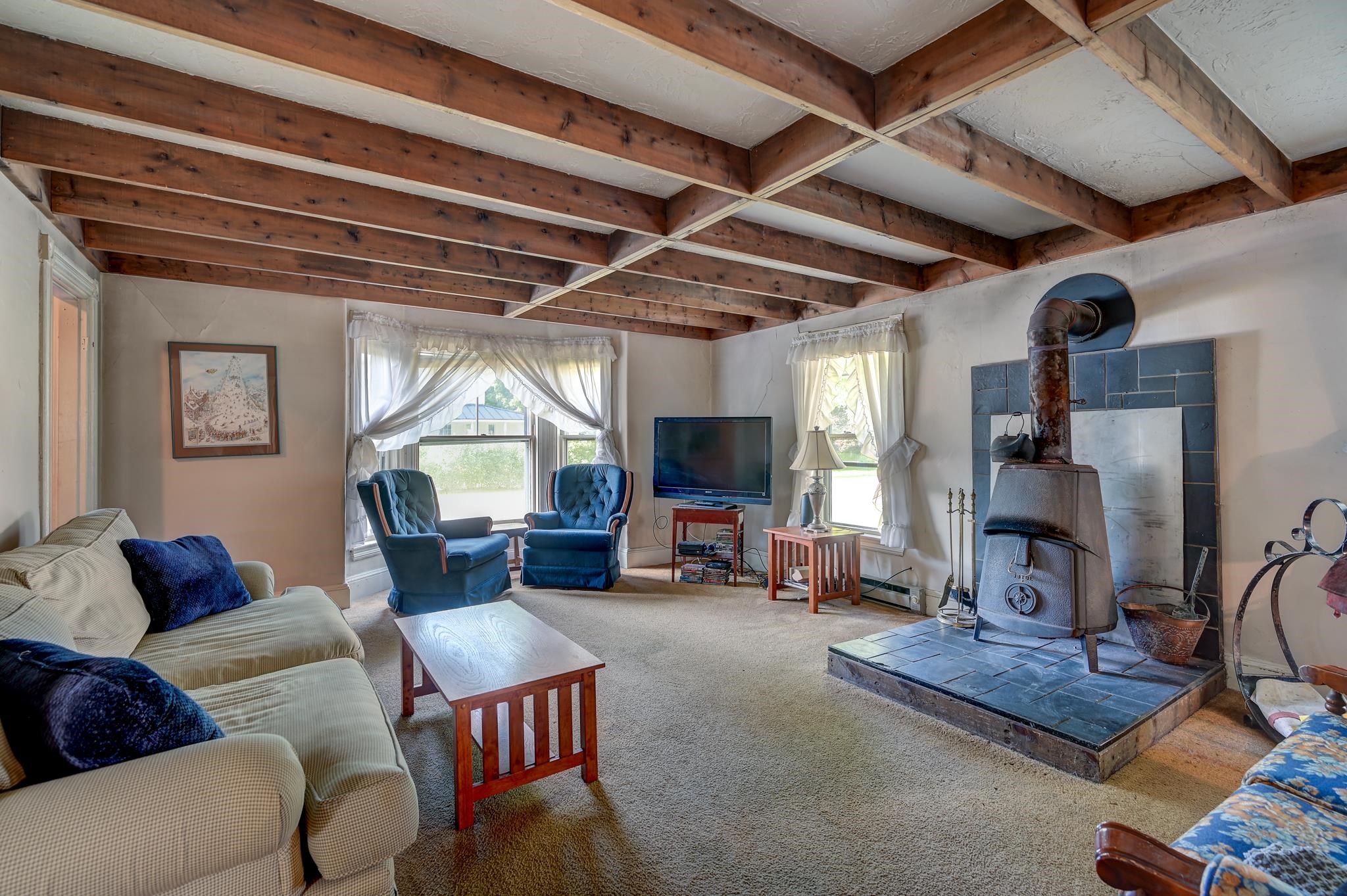 Living room with exposed beams, a freestanding wood stove, and blue armchairs.