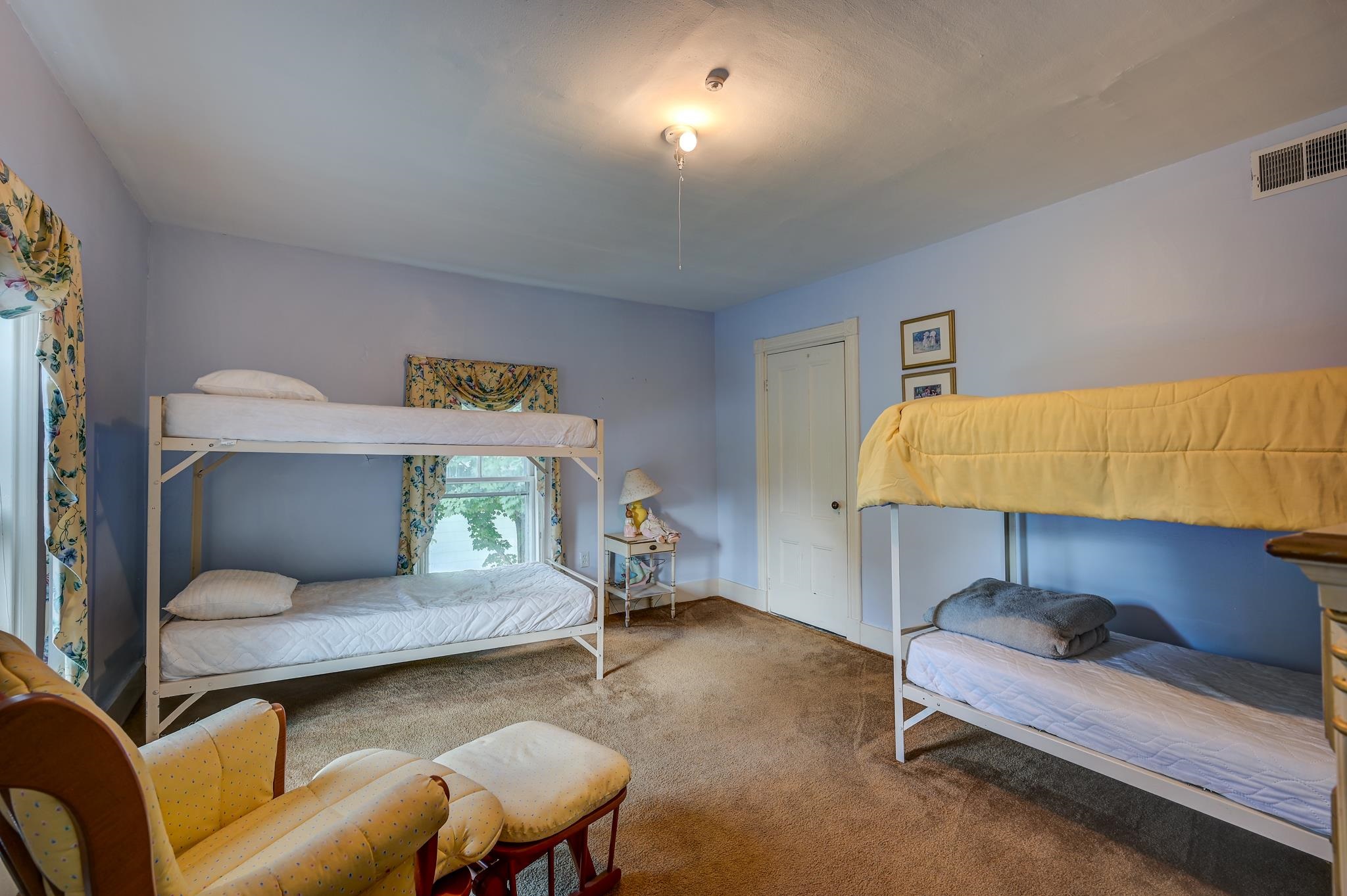 Bedroom with a white bunk bed, raised bed, floral curtains, and yellow armchair.