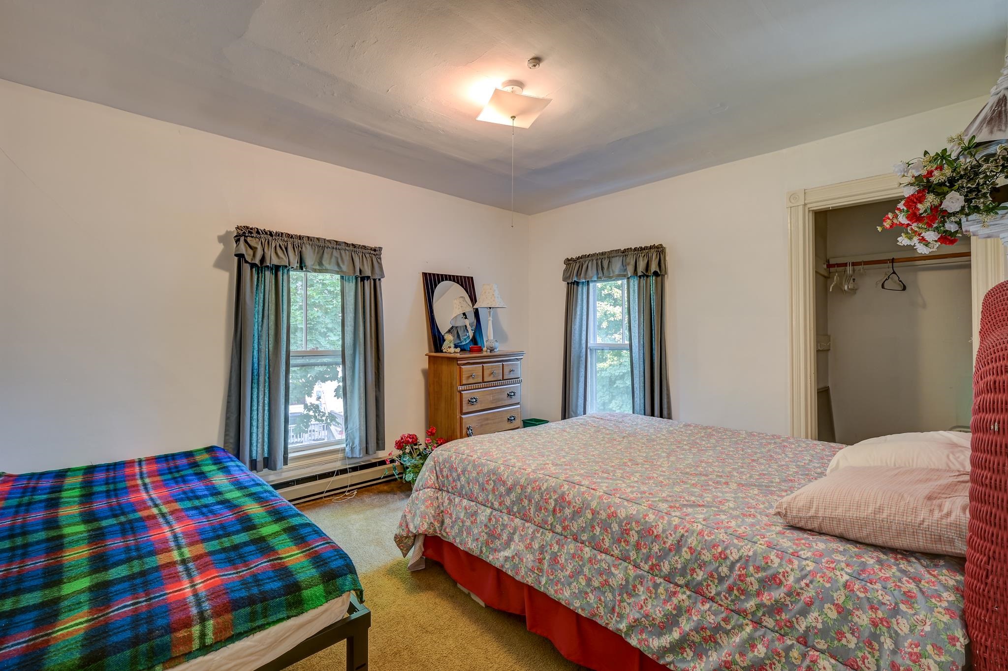Bedroom with two beds, a floral bedspread, colorful plaid blanket, and open closet.