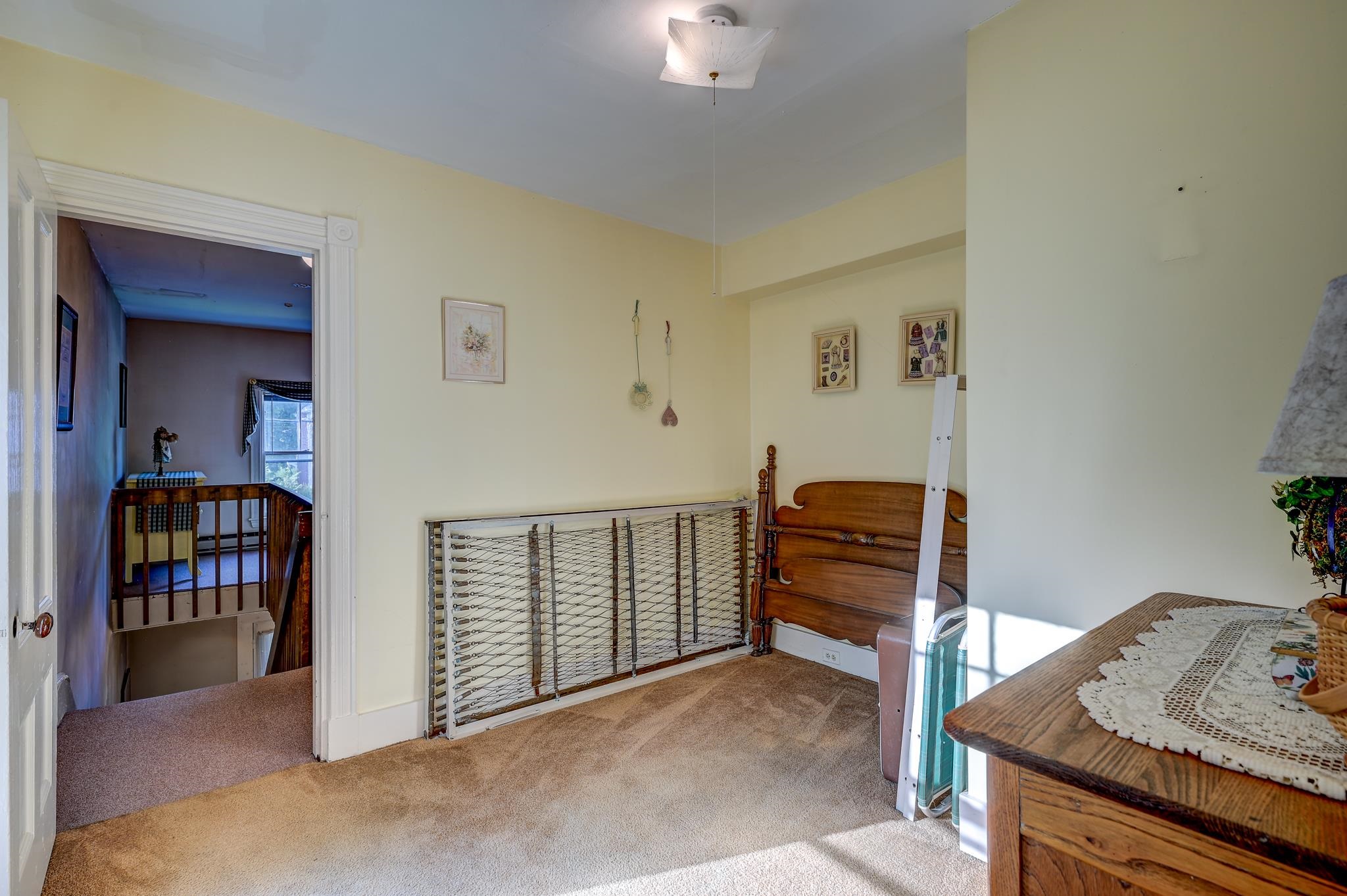 Upstairs bedroom with a wooden headboard, disassembled metal bed frame, and stairwell railing.