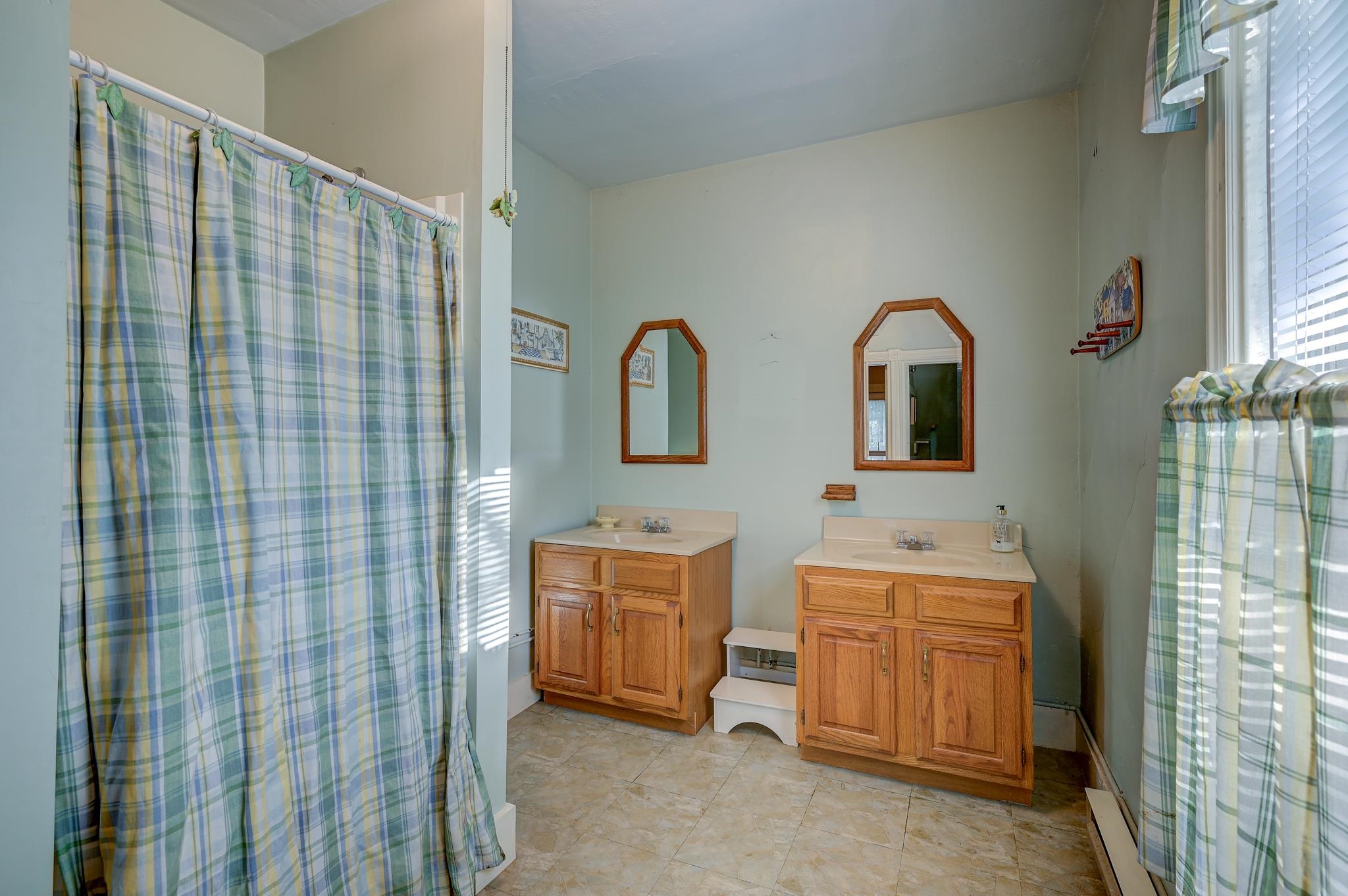 Bathroom with two wooden vanities, arched mirrors, and blue-green plaid shower curtains.