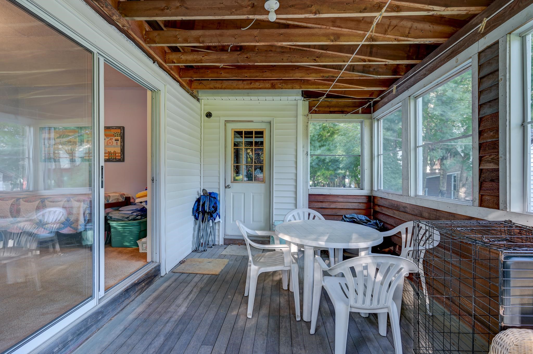 Enclosed porch with a white table and chairs, exposed wood ceiling, and screened windows.