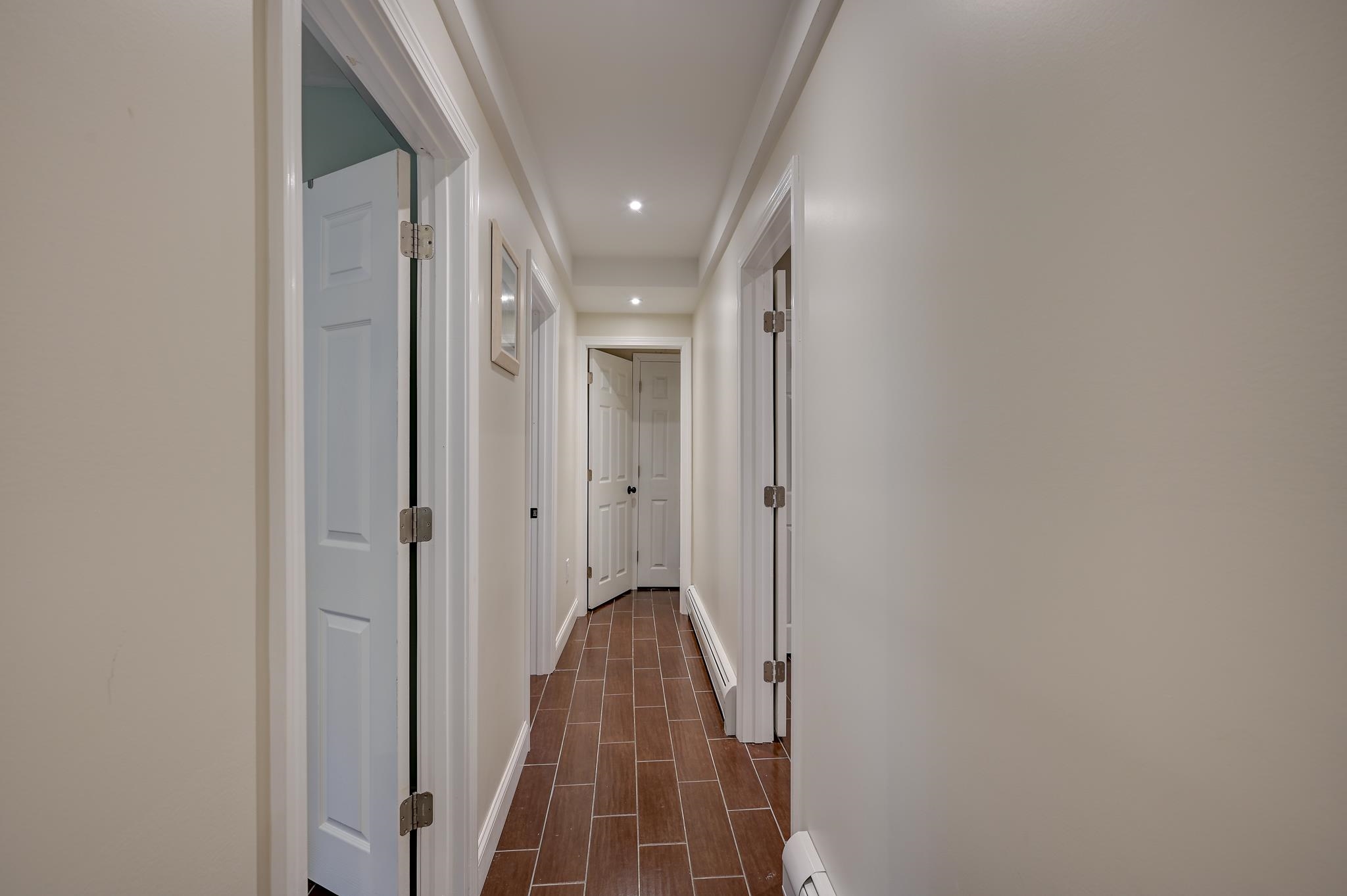 Hallway with brown tile flooring, multiple white doors, and recessed ceiling lights.