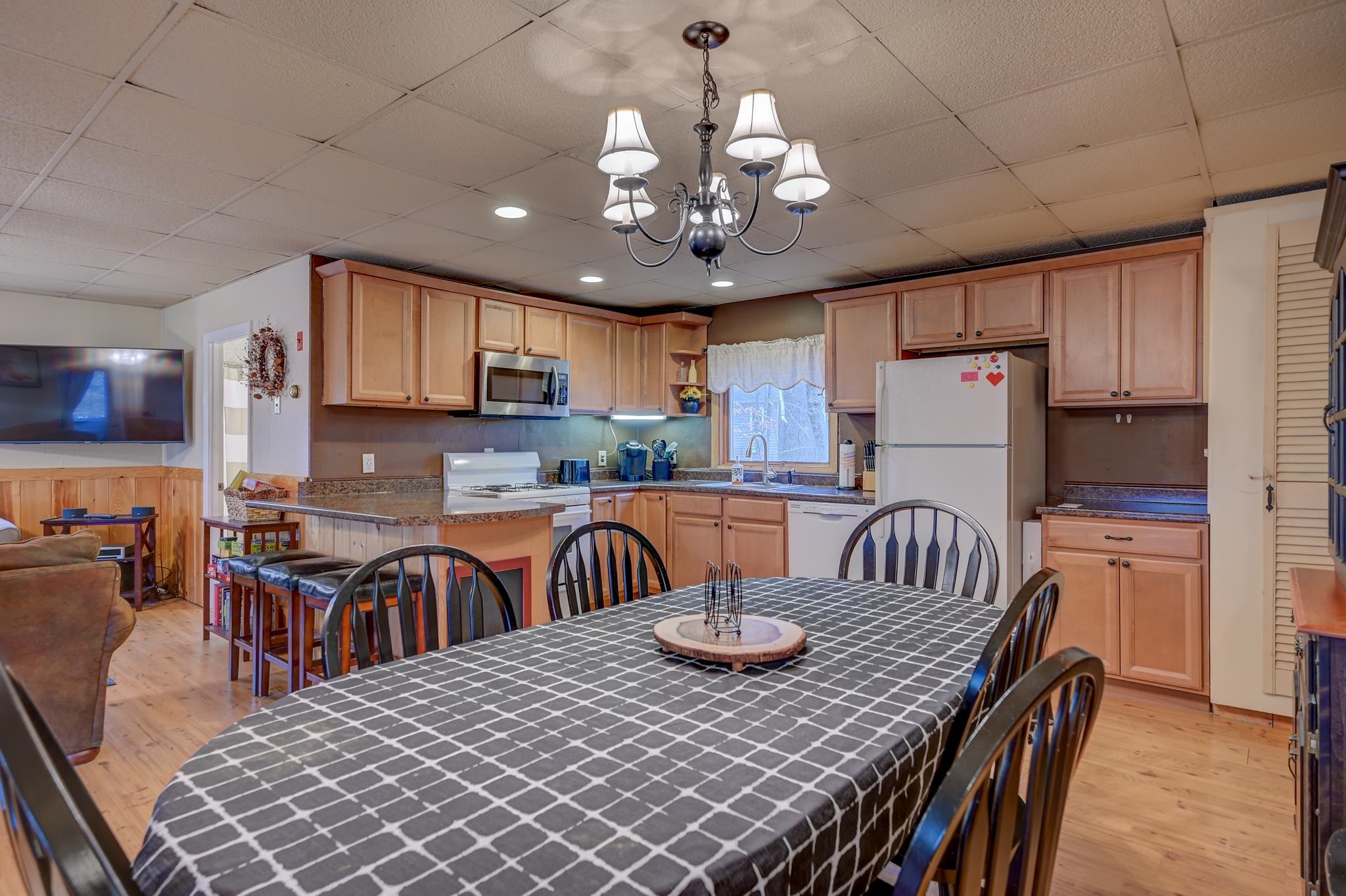 Kitchen and dining area with light wood cabinets, granite counters, and a large table beneath a chandelier.
