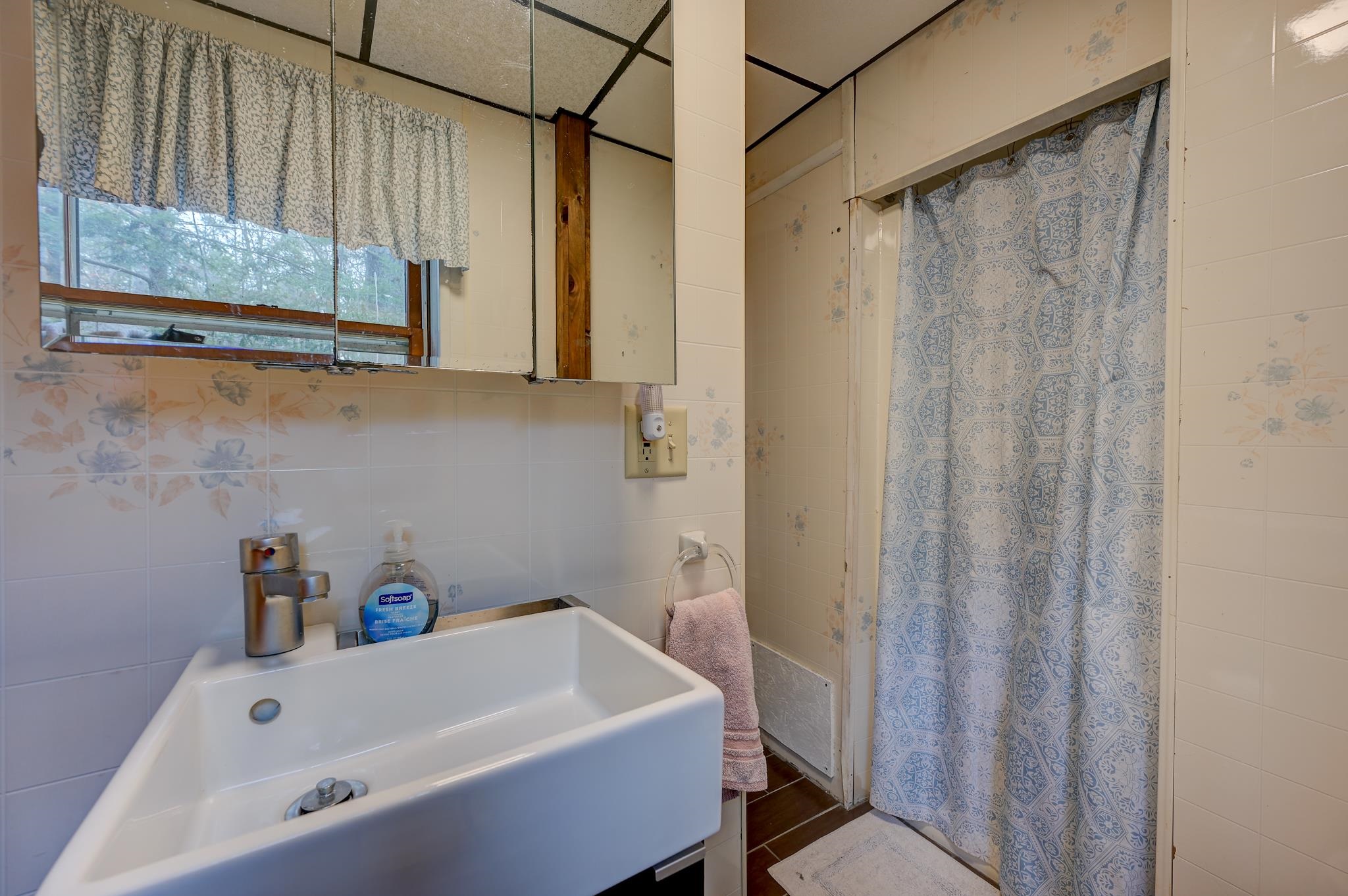 Bathroom with a white tub, mirrored cabinet, and blue patterned shower curtain.