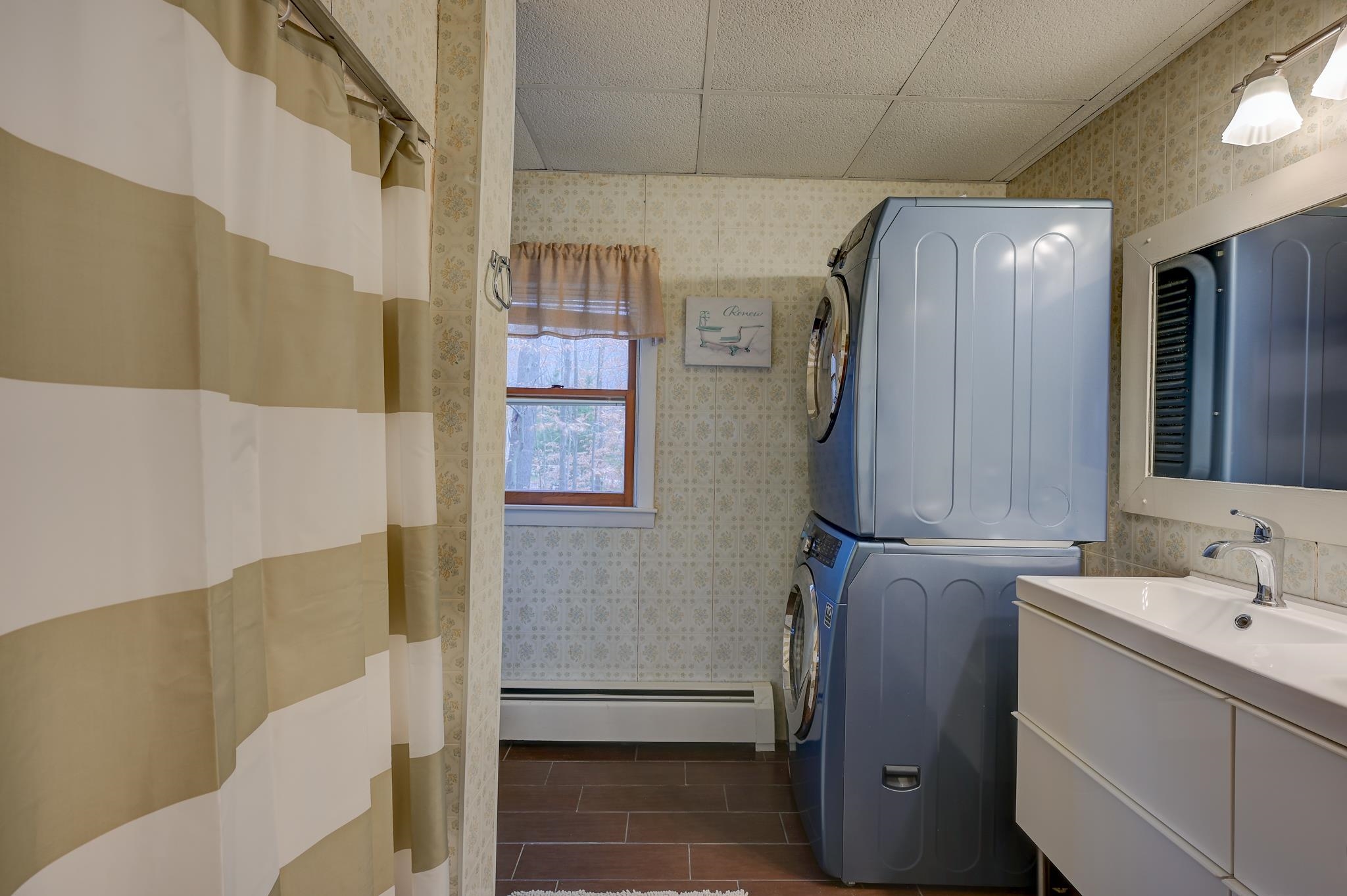 Laundry room with stacked washer and dryer beside a white sink vanity and striped shower curtain.