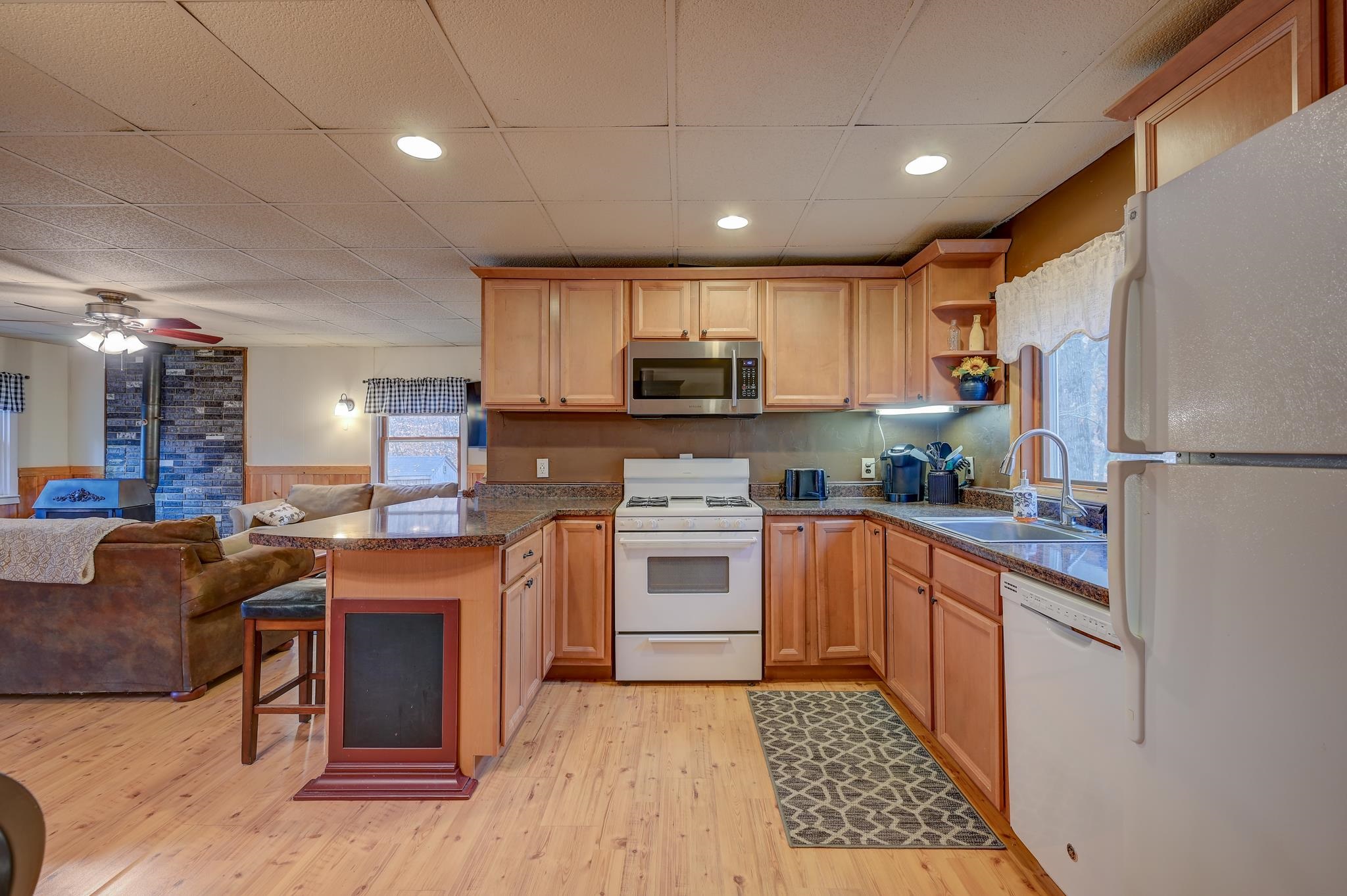 Open-plan kitchen with wood cabinets and granite island beside a living room with a brick fireplace.