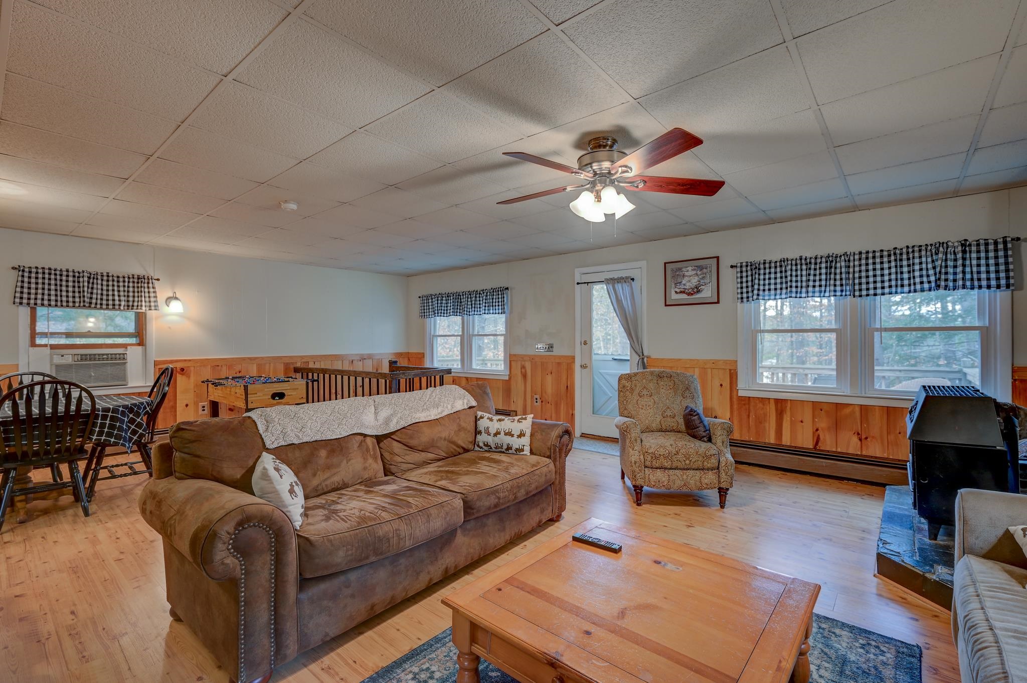 Furnished living room with a brown sofa, foosball table, wood stove, and checkered curtains.