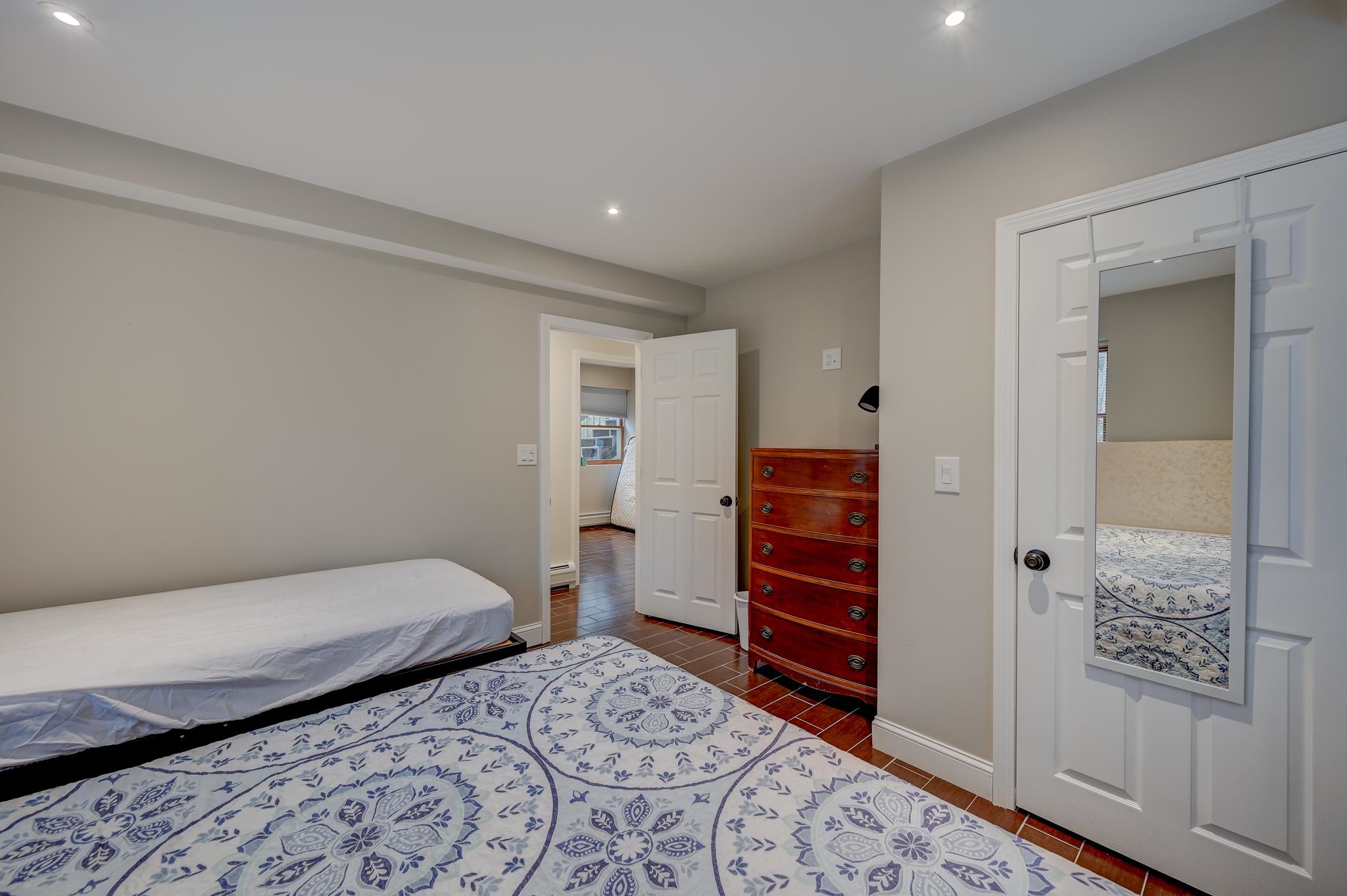 Bedroom with a blue-and-white patterned rug and wooden dresser beside an open doorway.