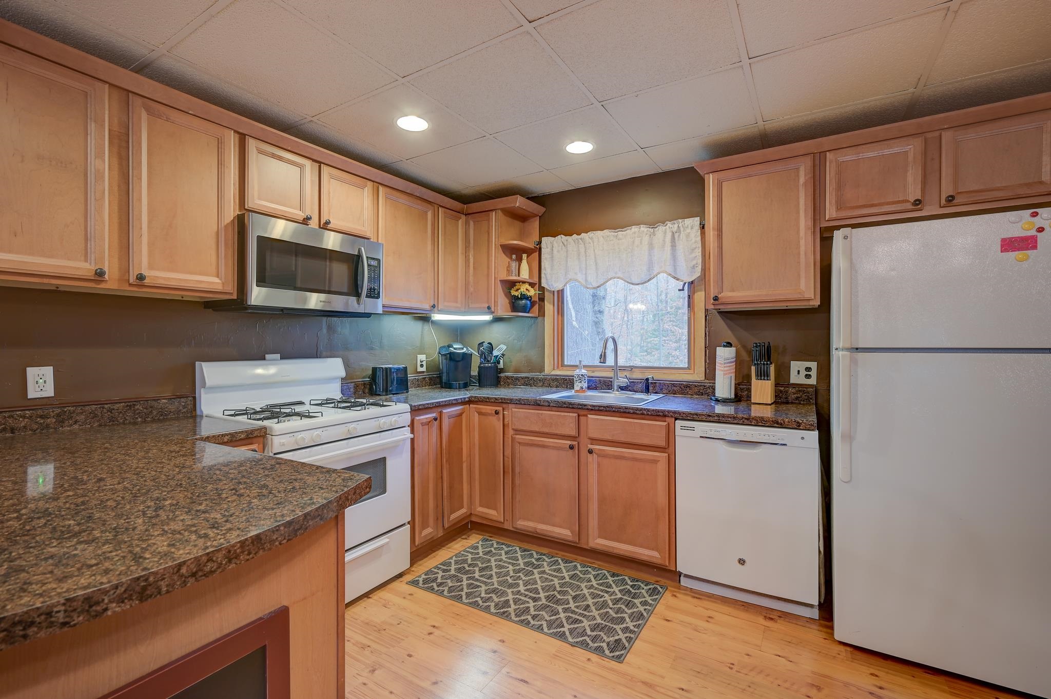 Kitchen with wood cabinets and granite counters, featuring a gas range and sink beneath a window.
