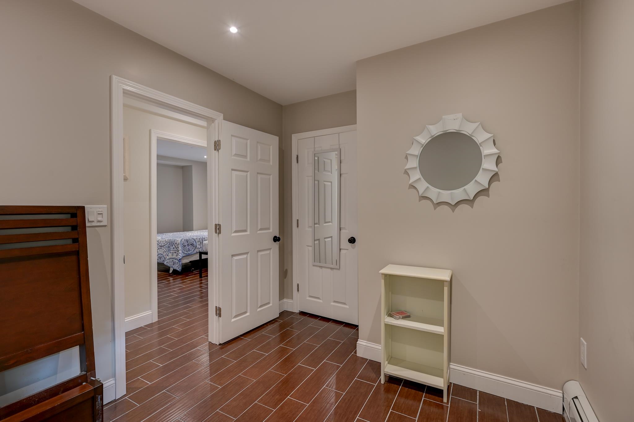 Hallway with brown tile flooring, white paneled doors, a sunburst mirror, and a bedroom visible through the open doorway.
