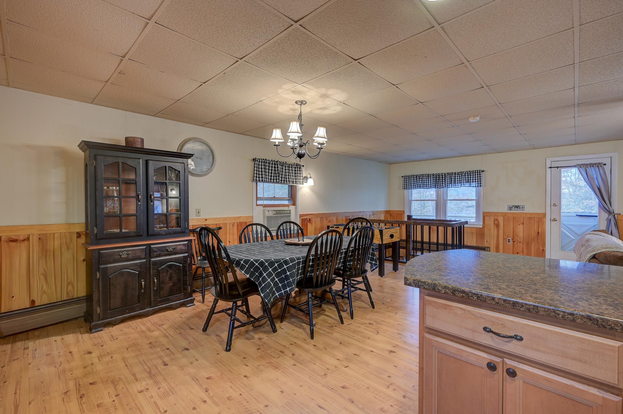 Dining area with a set table, dark china cabinet, wood flooring, and kitchen island.