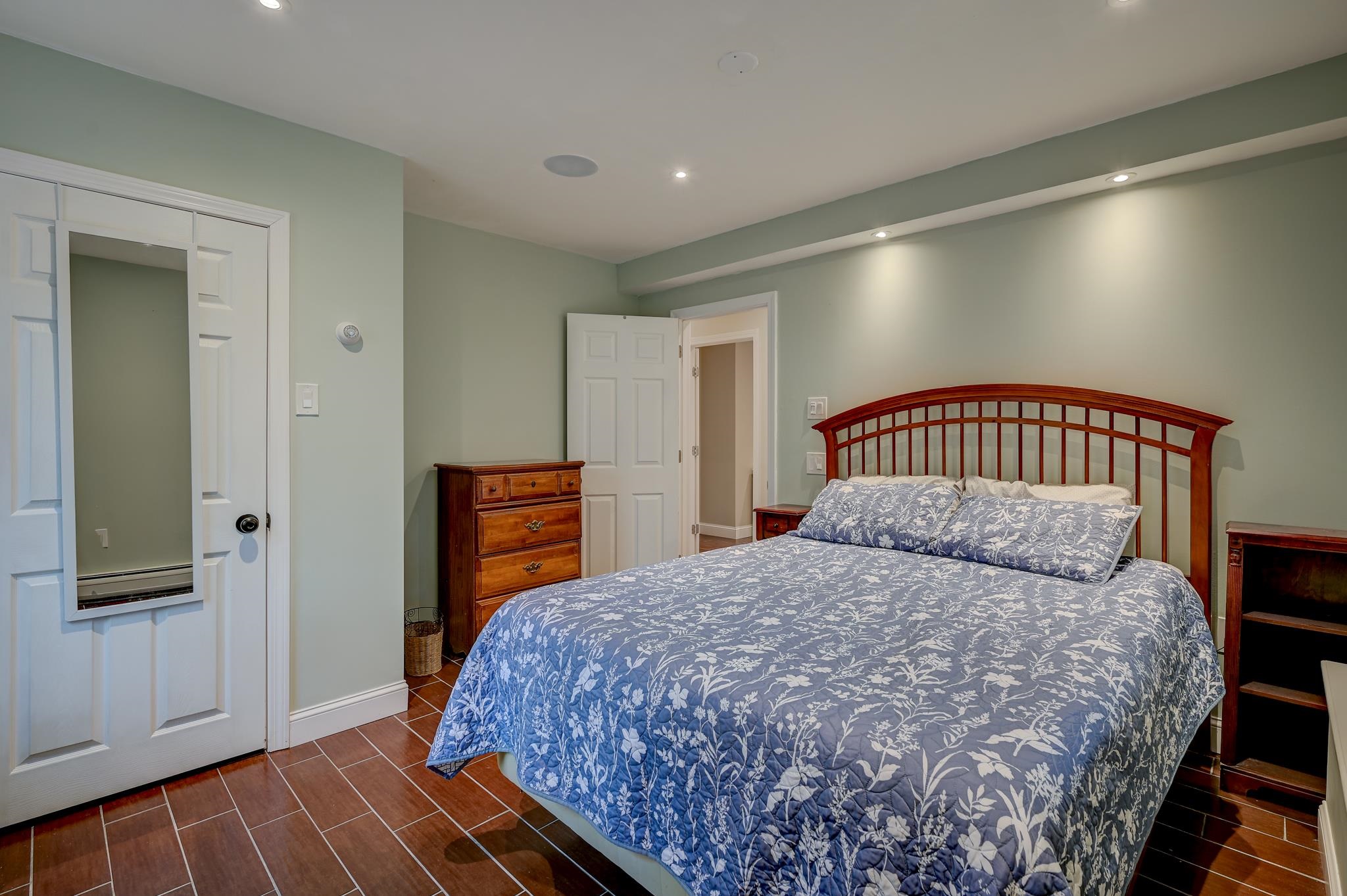 Furnished bedroom with blue floral bedding, a curved wooden headboard, and reddish-brown tile floors.