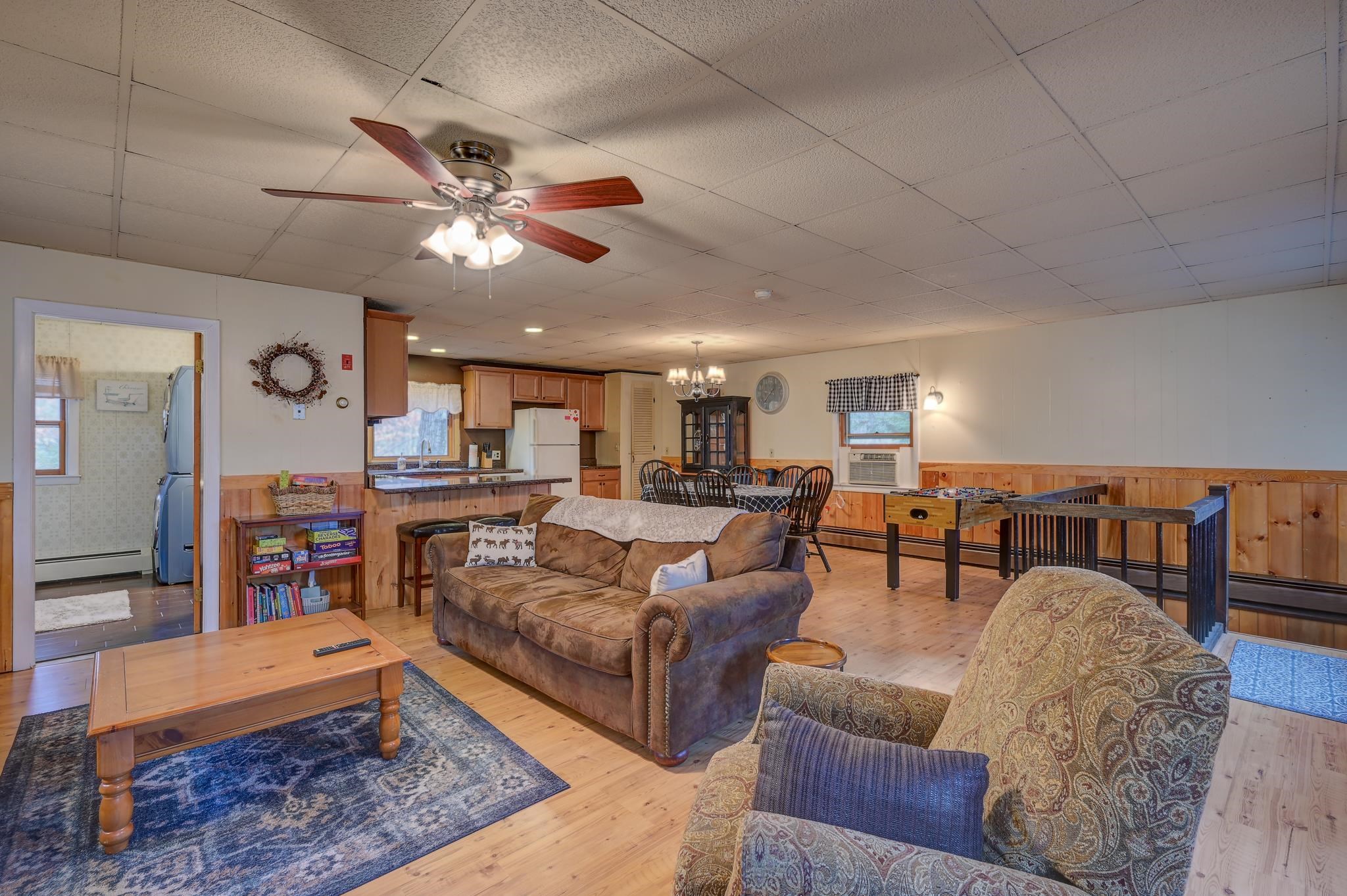 Open-plan living room with a brown sofa, adjoining kitchen, and game tables.