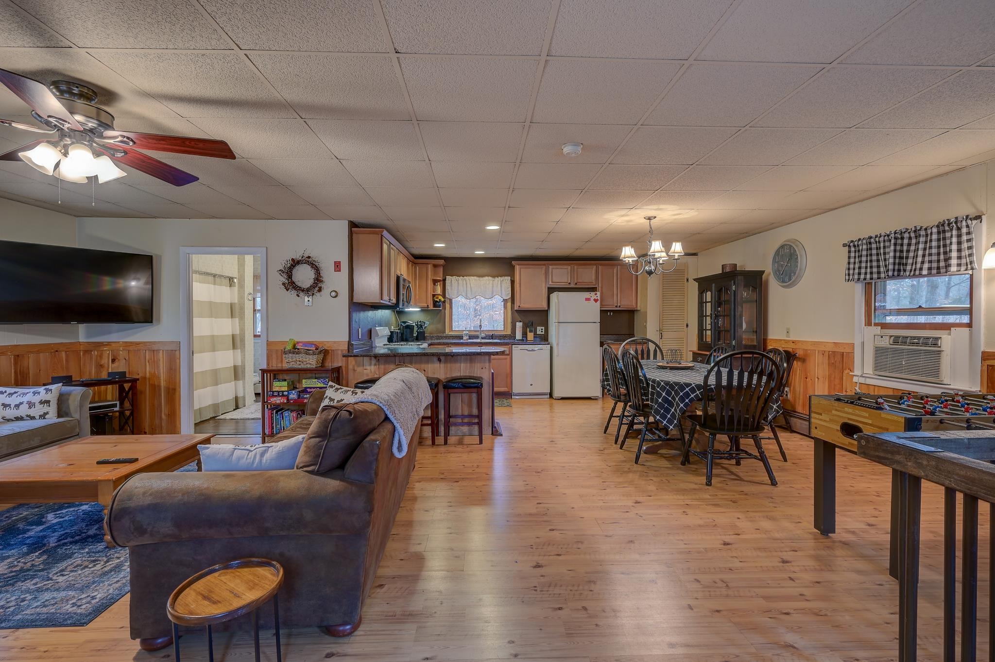 Open-plan living, dining, and kitchen area with wood floors, a breakfast bar, and foosball table.
