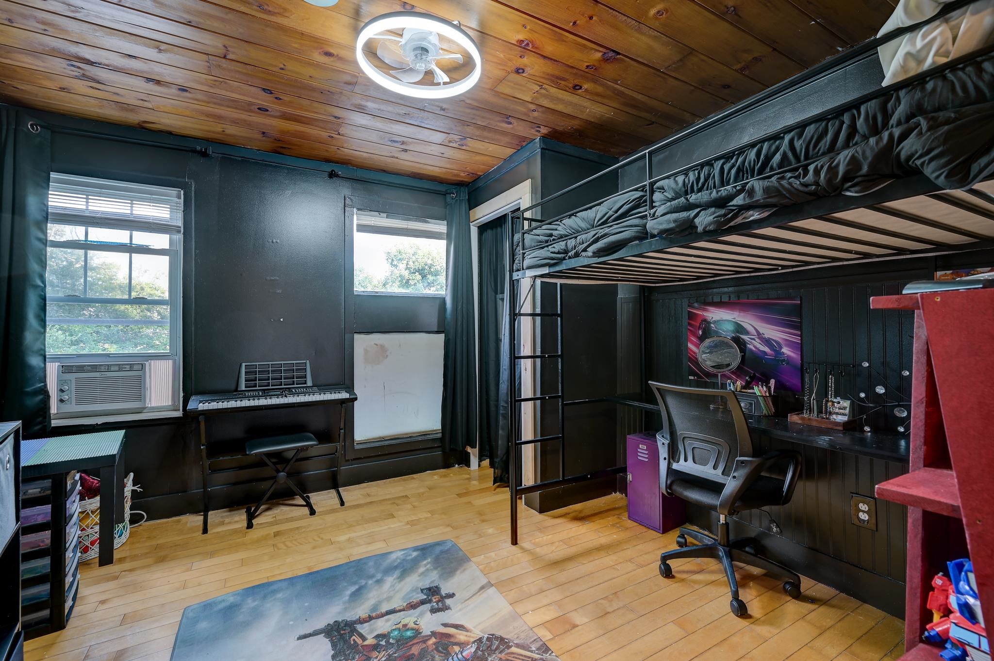Bedroom with a black loft bed, desk, keyboard, and warm wood ceiling.