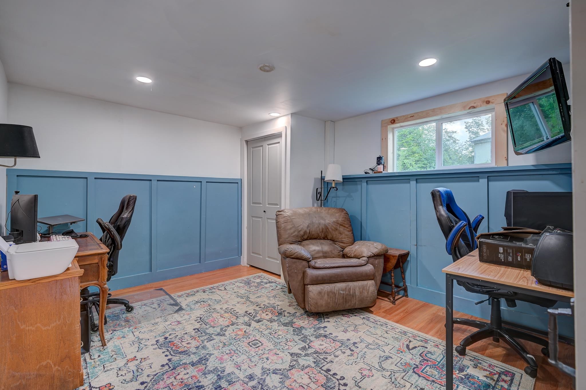 Home office with blue paneled walls, two computer desks, and a brown leather recliner.