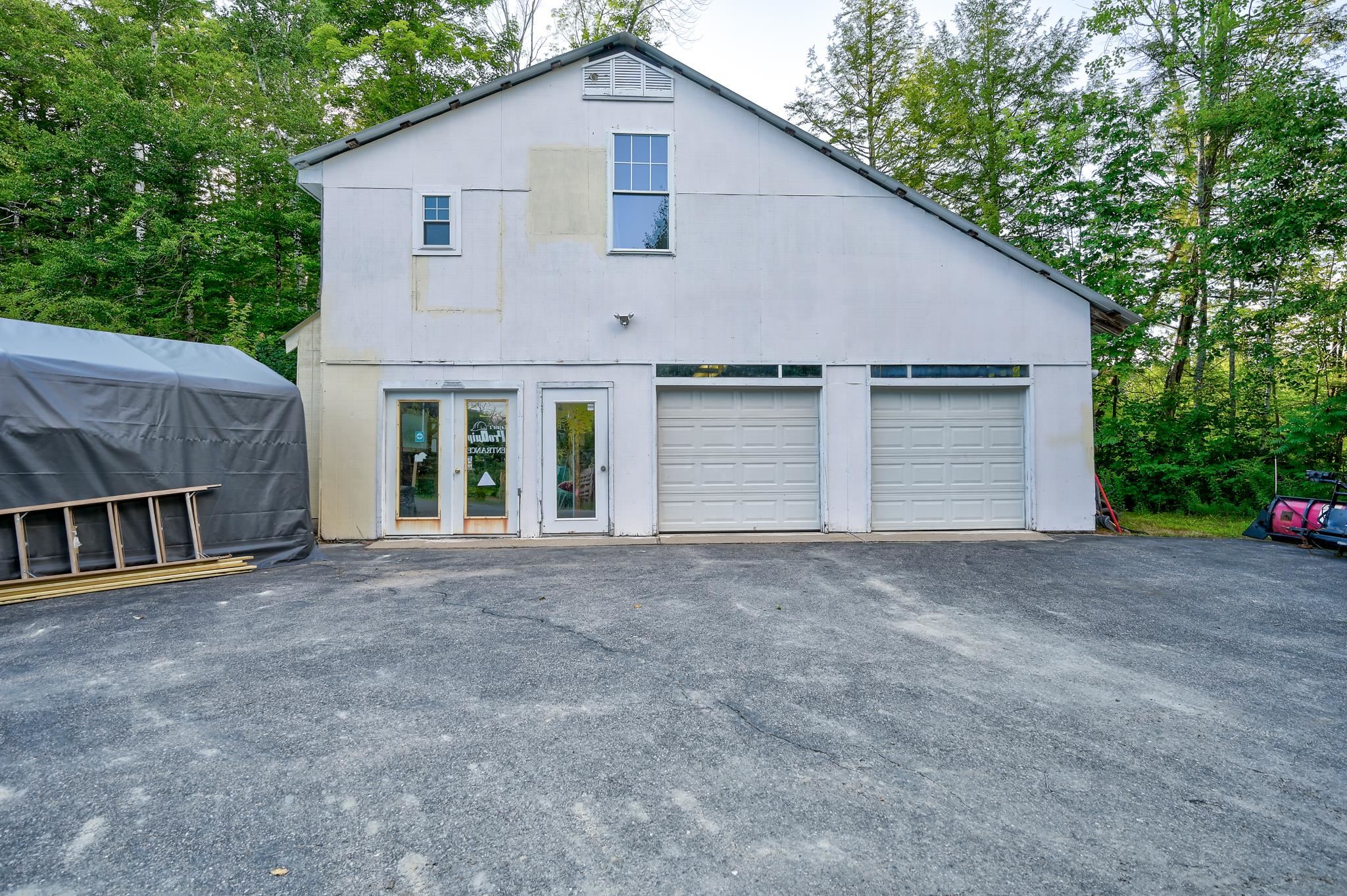 White barn-style building with two garage doors and glass entry doors, surrounded by trees.