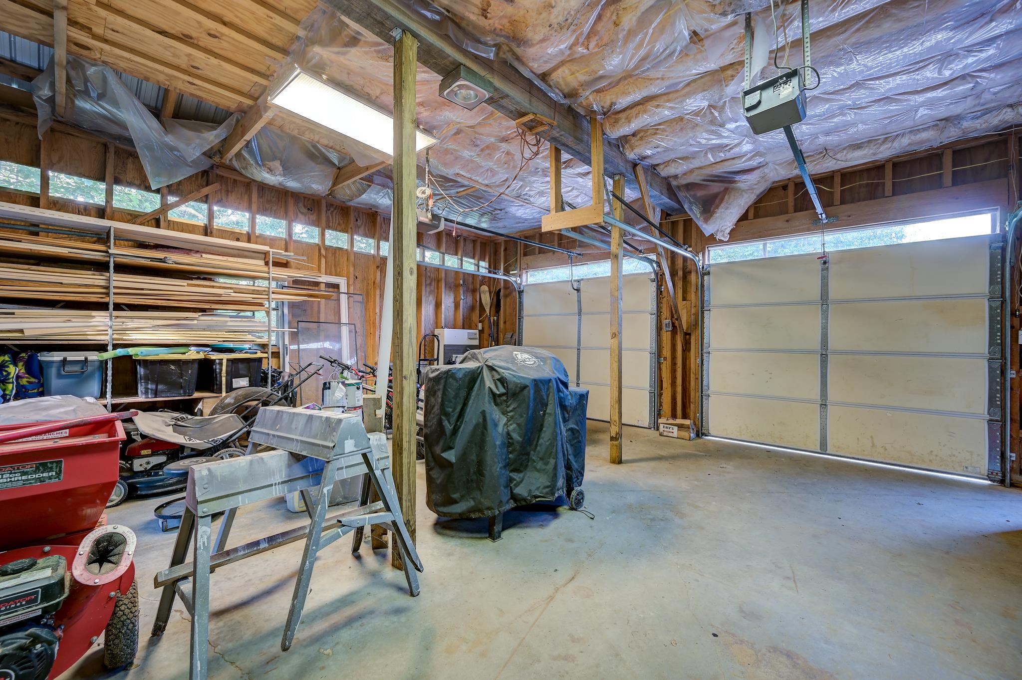 Two-bay garage workshop with lumber racks, tools, and equipment stored around the open floor.