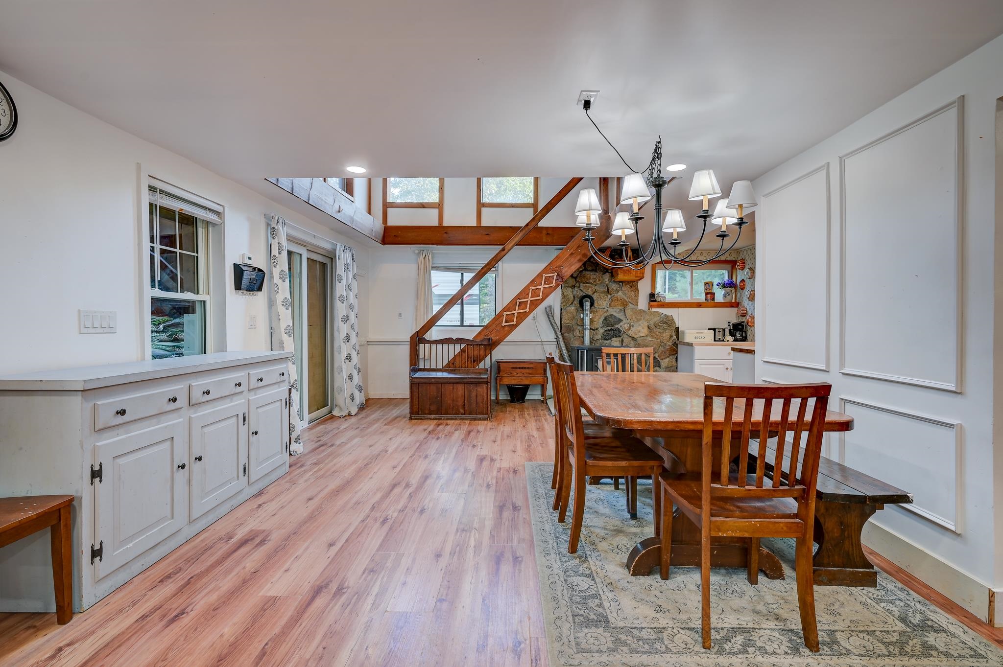 Dining area with a wooden table, stone fireplace, and open staircase to a loft.