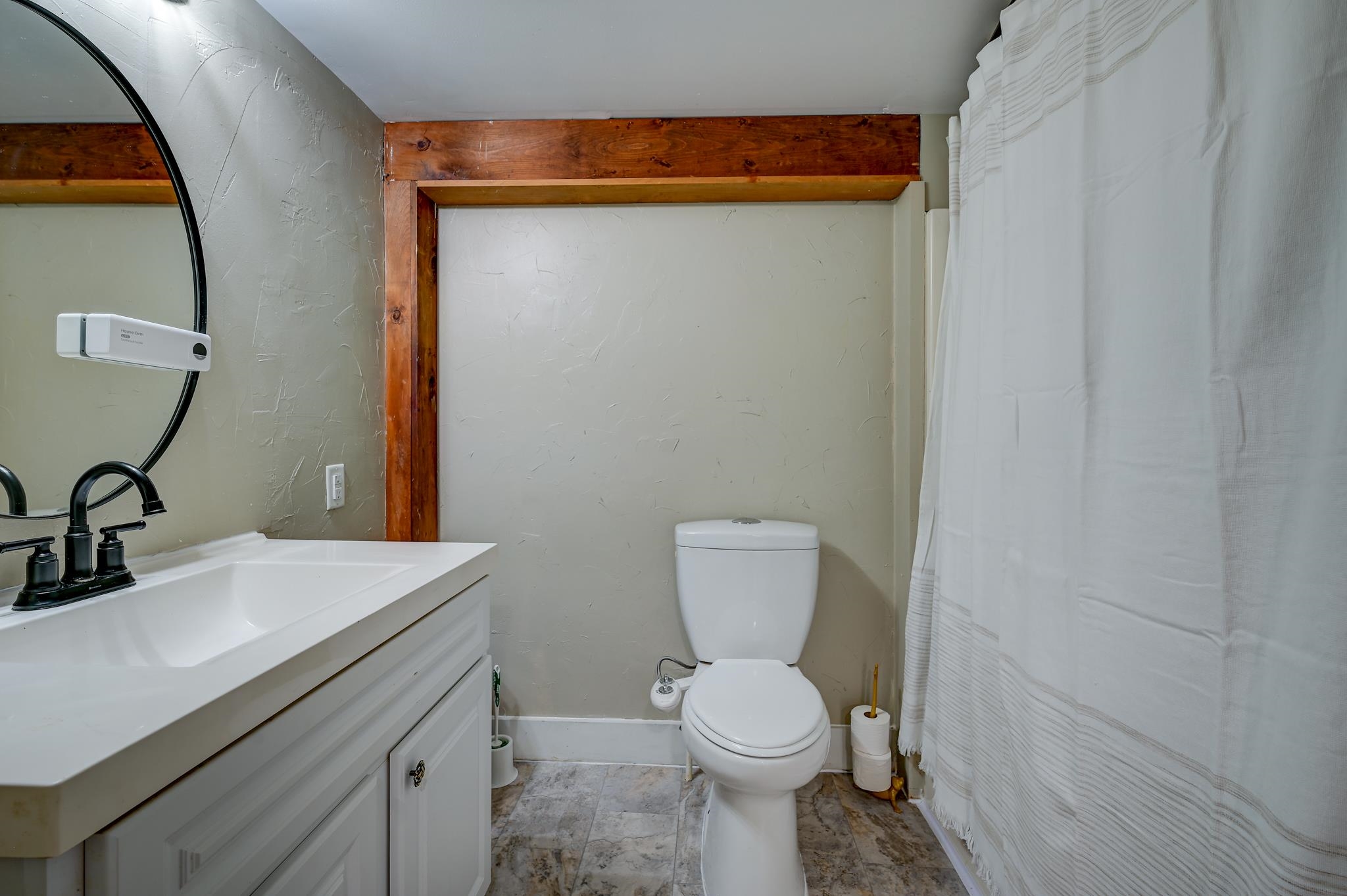 Bathroom with a white vanity, toilet, striped shower curtain, and exposed wood beams.
