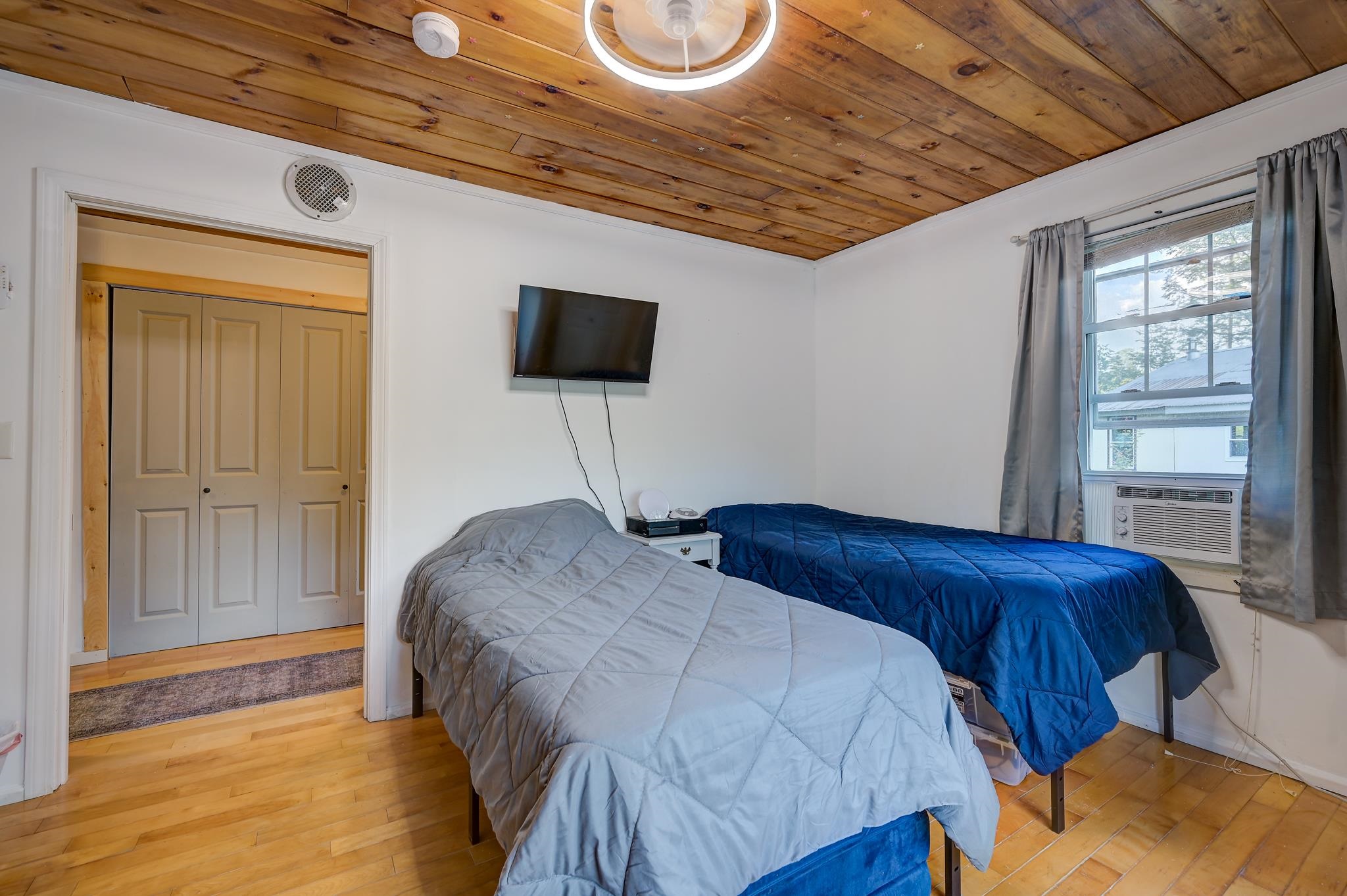 Bedroom with two single beds, a wood-plank ceiling, and a window air conditioner.
