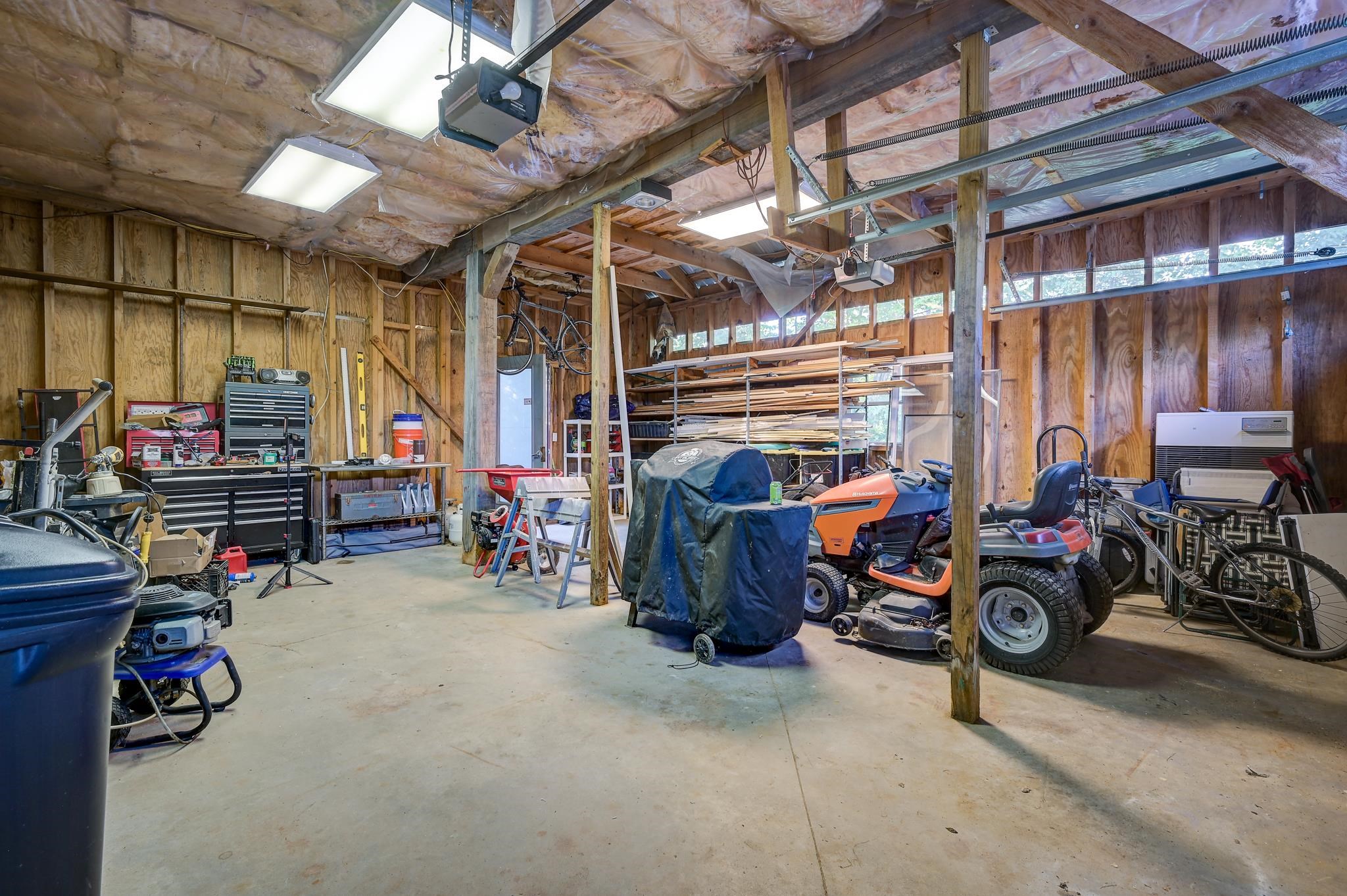 Wooden garage workshop with tool chests, lumber racks, lawn tractors, and bicycles.