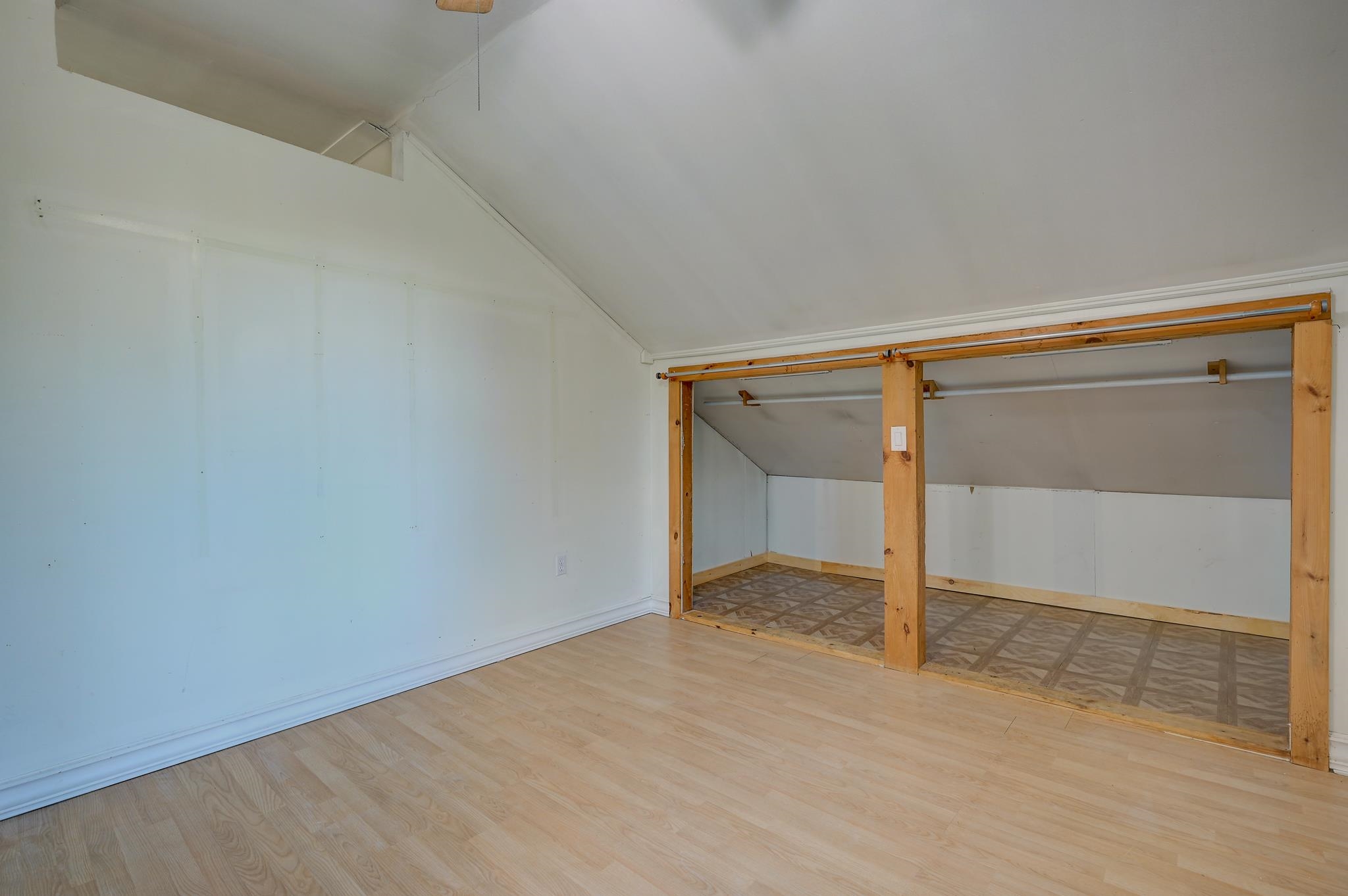 Empty attic room with sloped ceiling and open built-in closet.