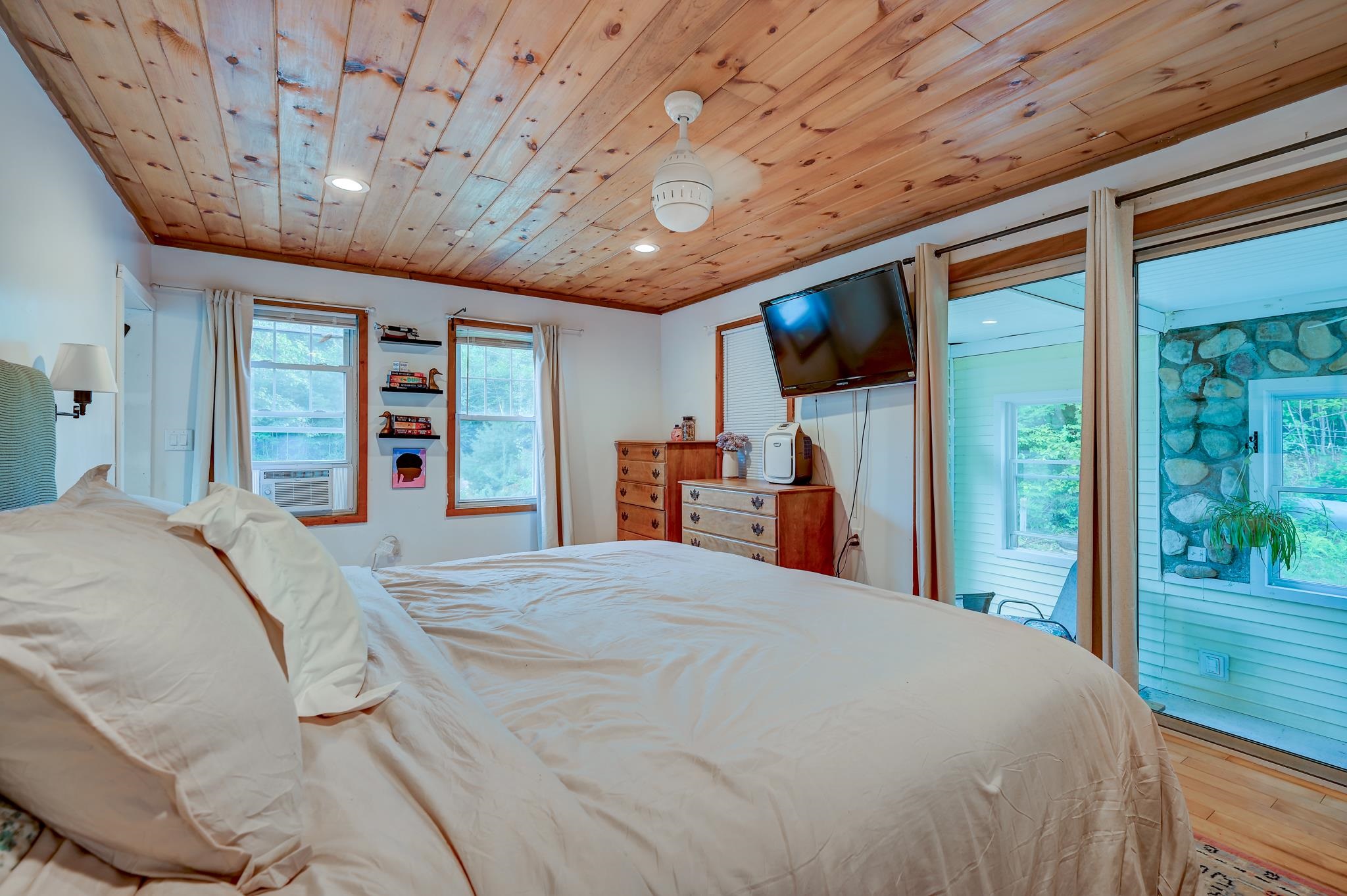 Bedroom with a knotty wood ceiling, large bed, and sliding glass doors to an enclosed porch.