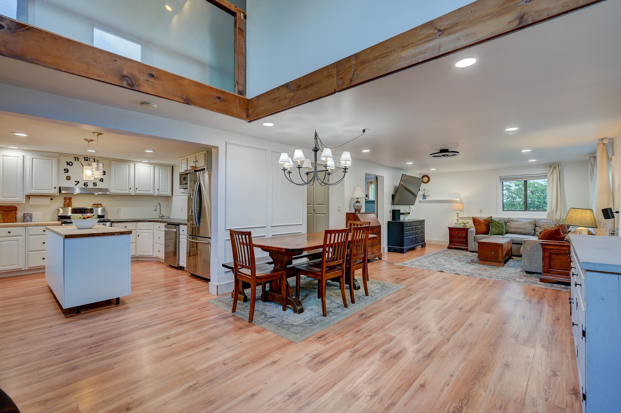 Open-plan kitchen, dining area, and living room with white cabinetry and exposed timber framing.
