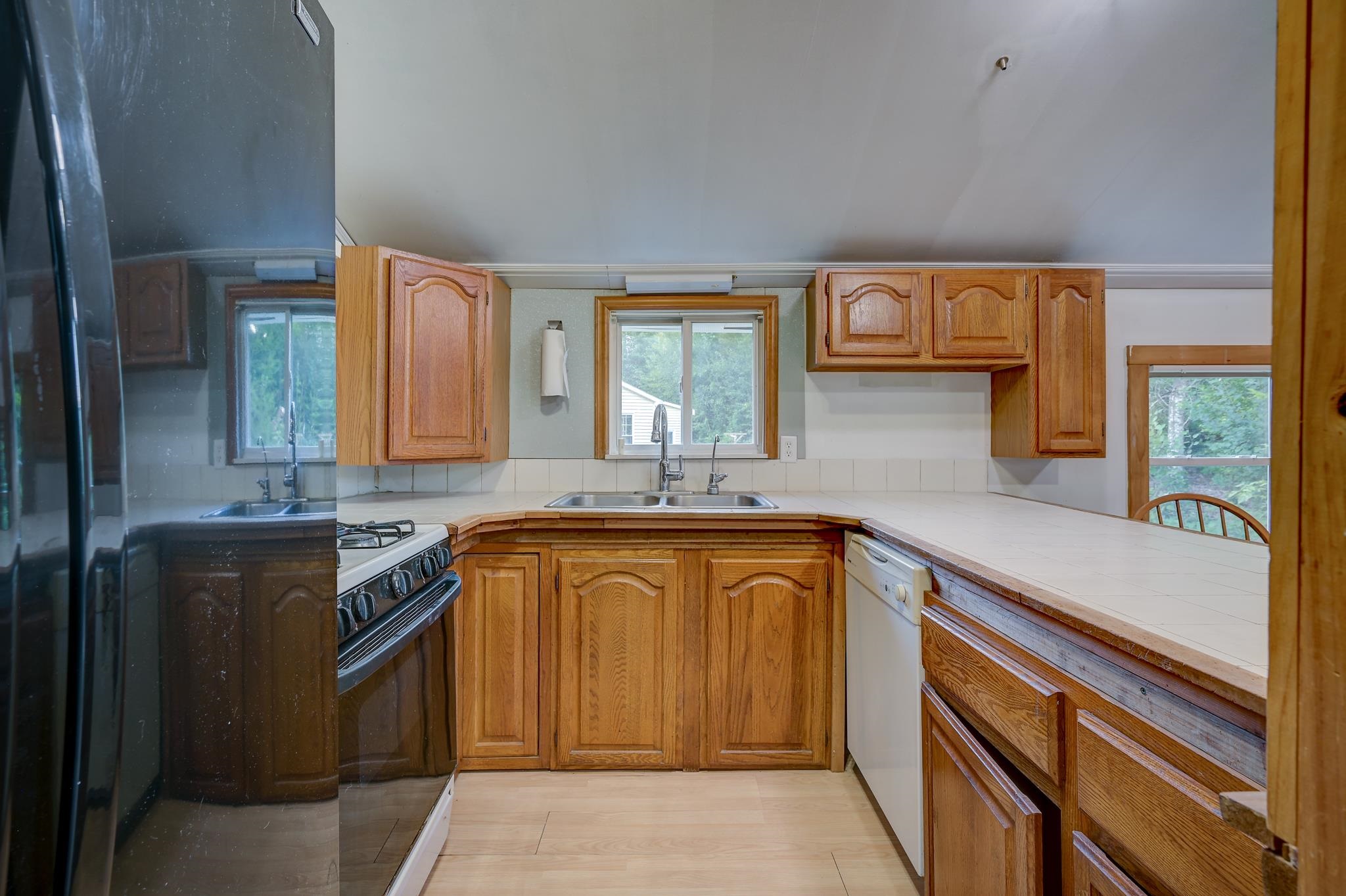 Kitchen with honey-colored wood cabinets, tiled counters, a double sink, gas range, and dishwasher.