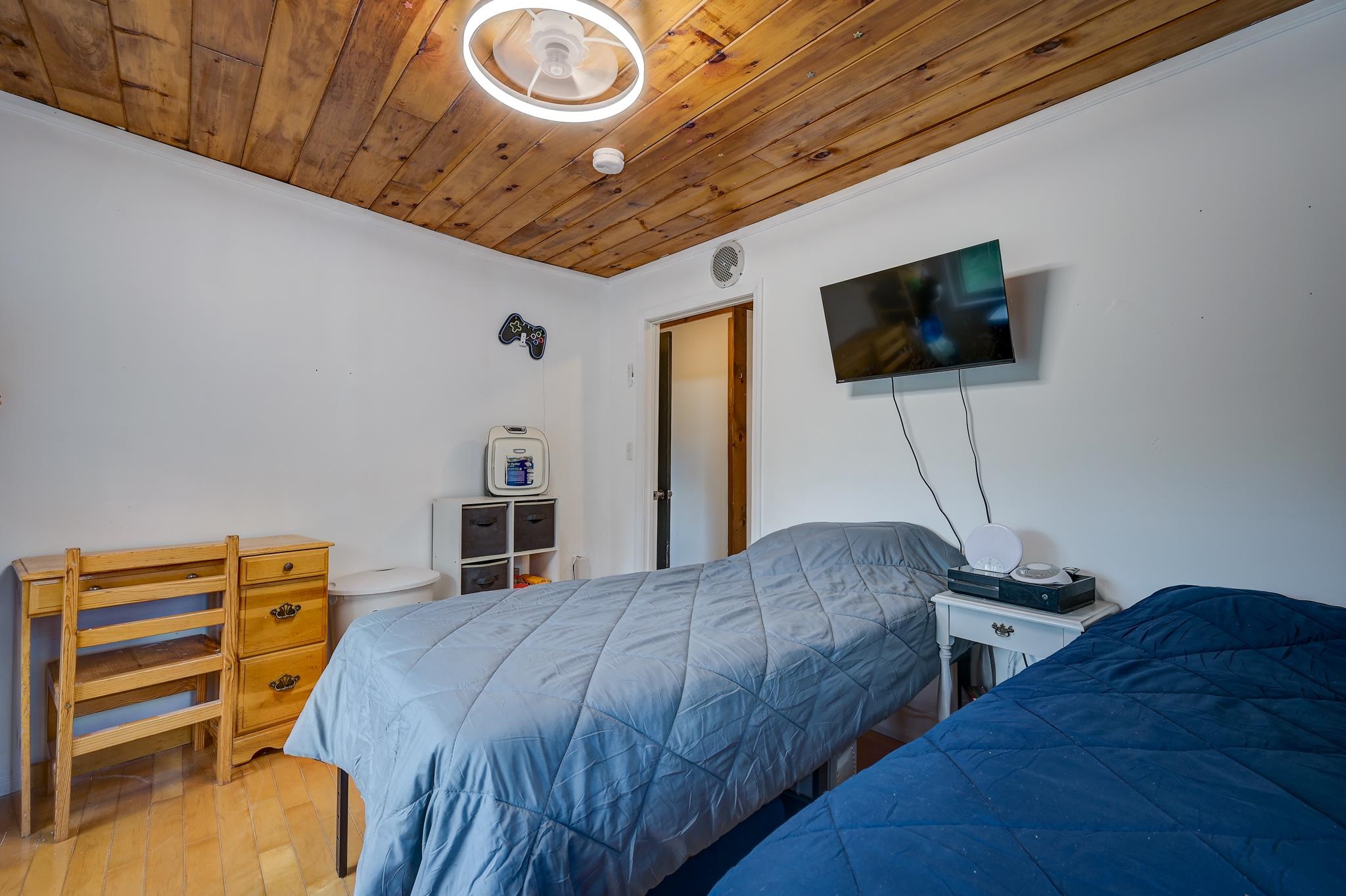 Bedroom with two beds beneath a warm wood plank ceiling and a wall-mounted television.