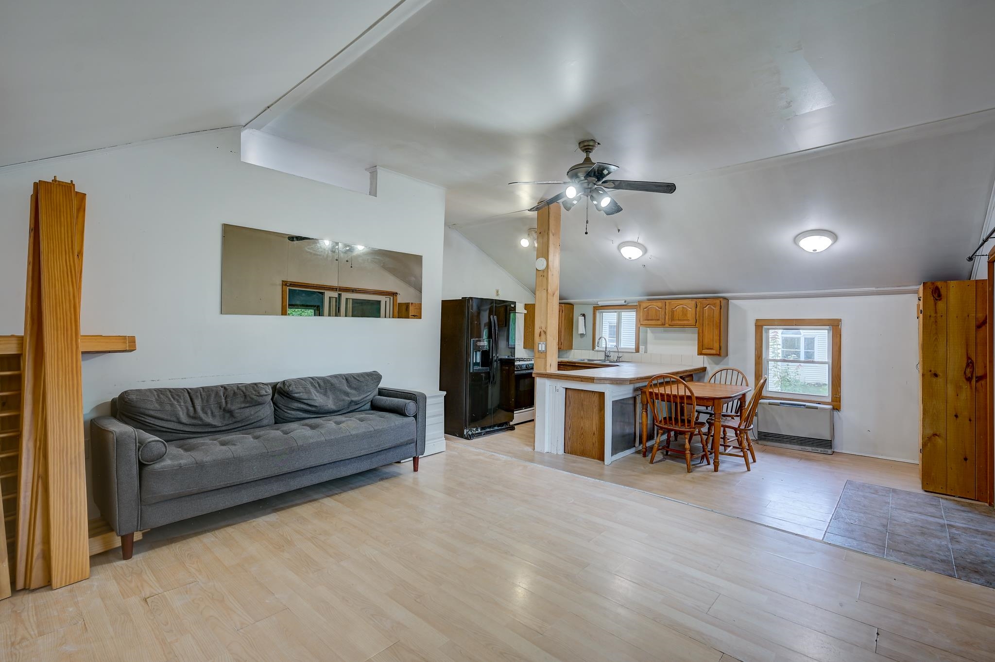 Open living room and kitchen with gray sofa, wood cabinets, breakfast island, and dining table.