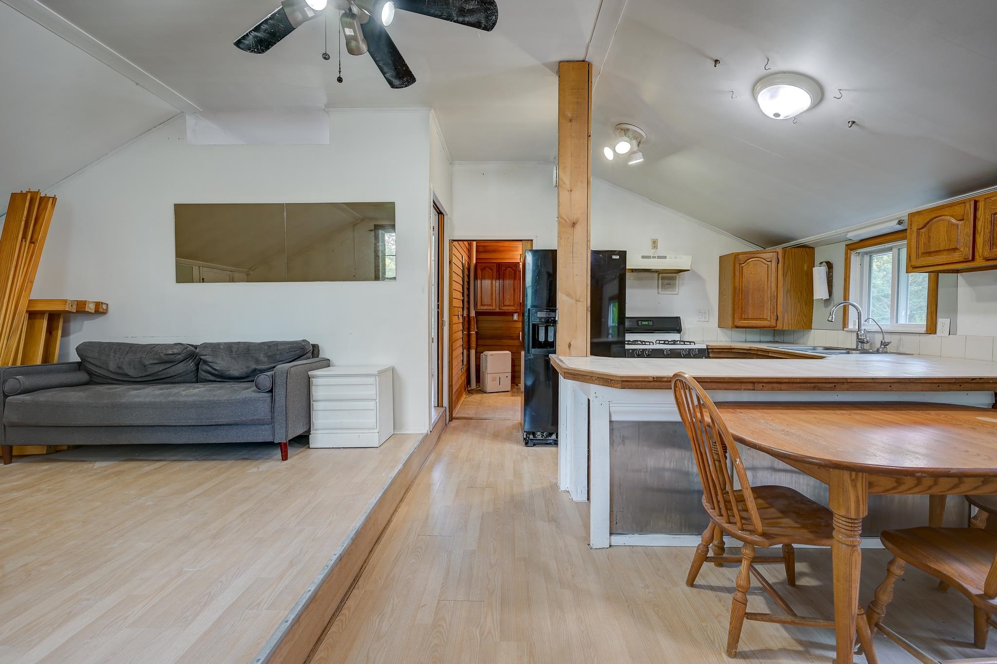 Open-plan kitchen and living area with a gray sofa, wood cabinets, and dining table.