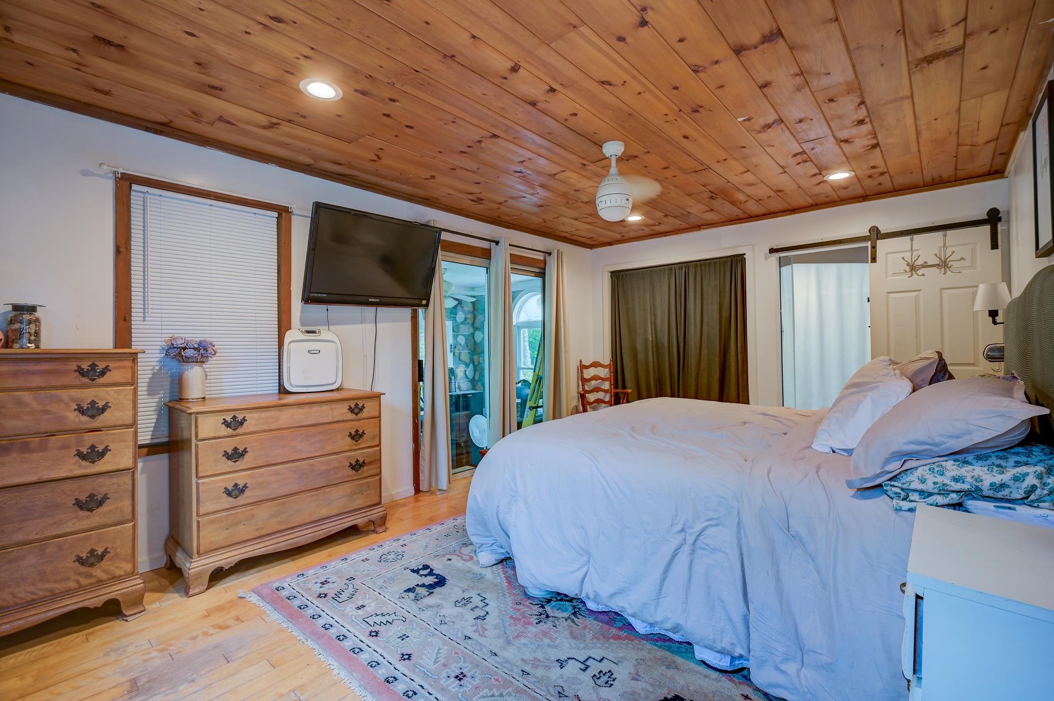 Bedroom with a large bed, pine-plank ceiling, wooden dressers, and patterned rug.