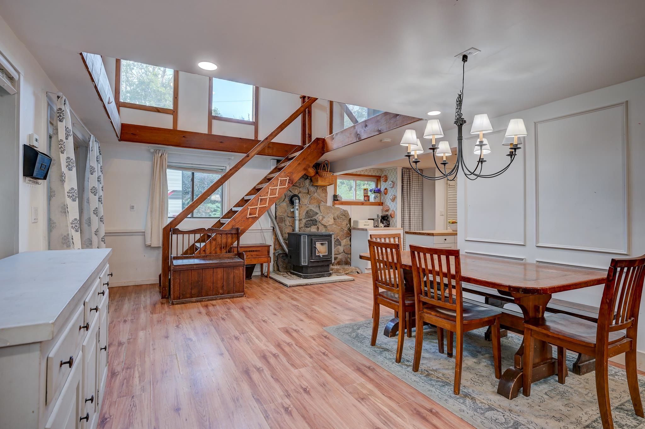 Dining area with a wood staircase, stone fireplace and wood stove, and a large wooden table.