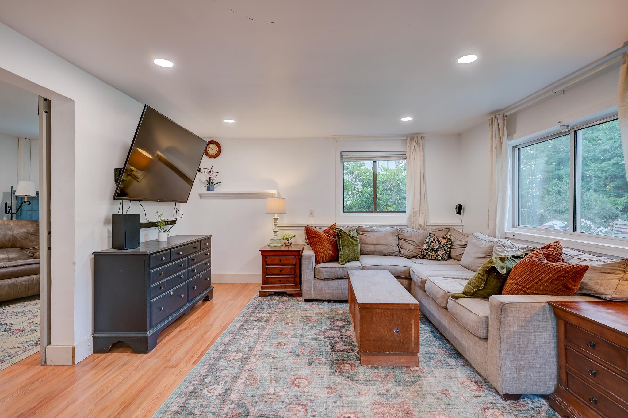 Living room with a gray sectional, patterned rug, wooden coffee table, and large windows overlooking greenery.