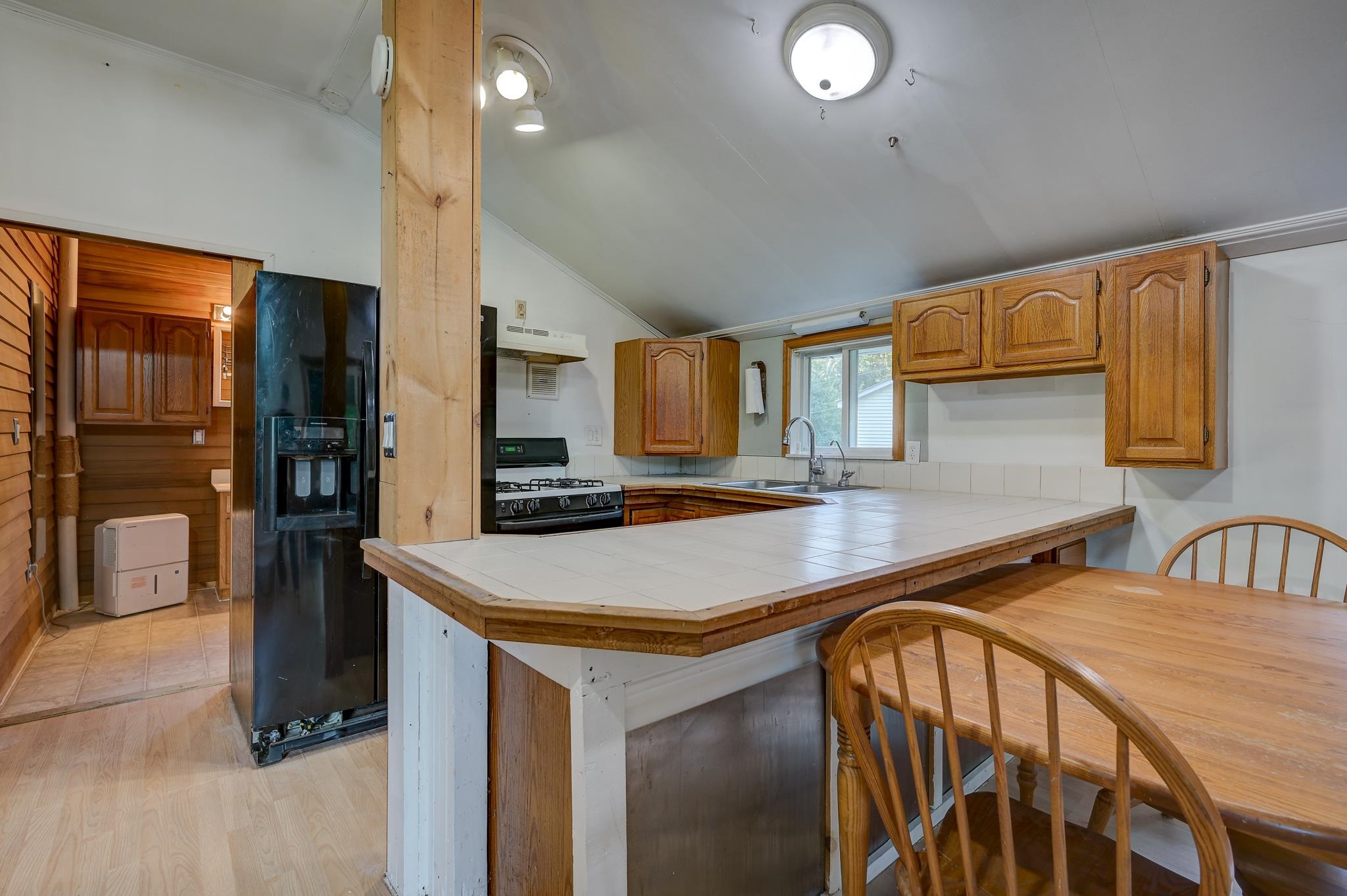 Kitchen with wood cabinets, tiled peninsula, black refrigerator, and adjoining wooden dining table.