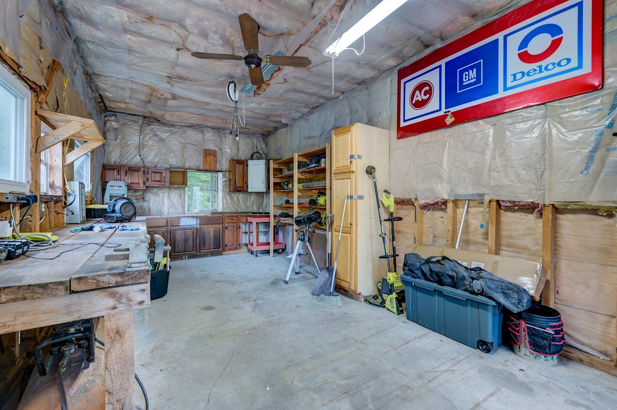 Garage workshop with a wooden workbench, storage cabinets, tools, and a large AC, GM, and Delco sign.