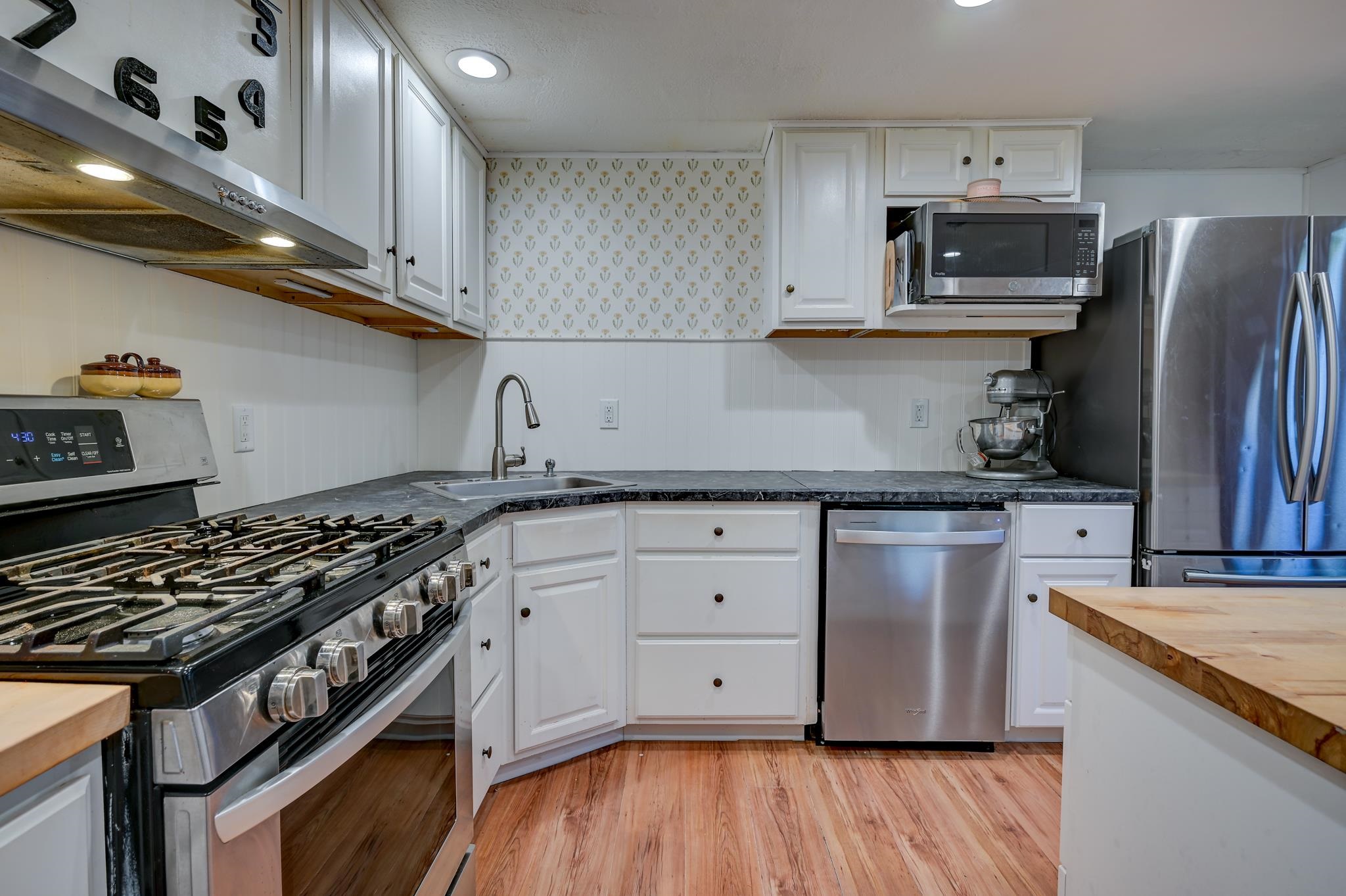 Kitchen with white cabinets, a large stainless steel gas range, and patterned wallpaper above the sink.