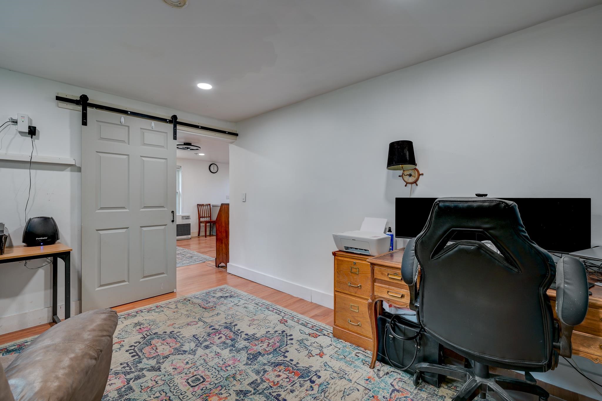 Home office with a black desk chair, barn-style sliding door, and patterned rug.